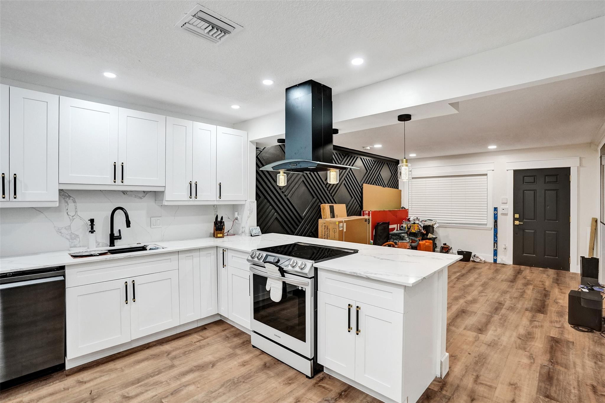 White kitchen with a large island, black geometric backsplash, and moving boxes near the entry.