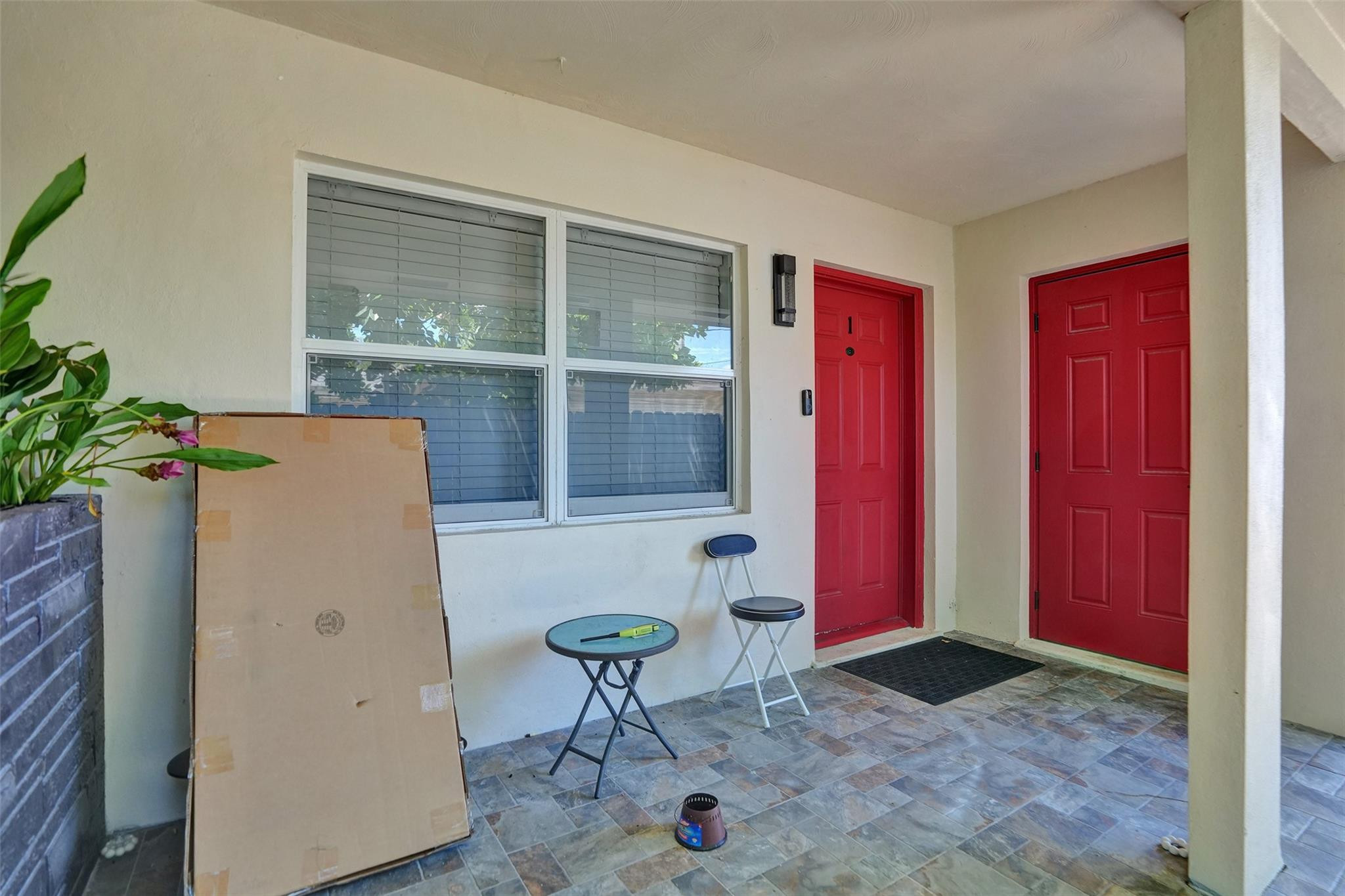 Covered entry with two red doors, a large window, and a tiled porch floor.