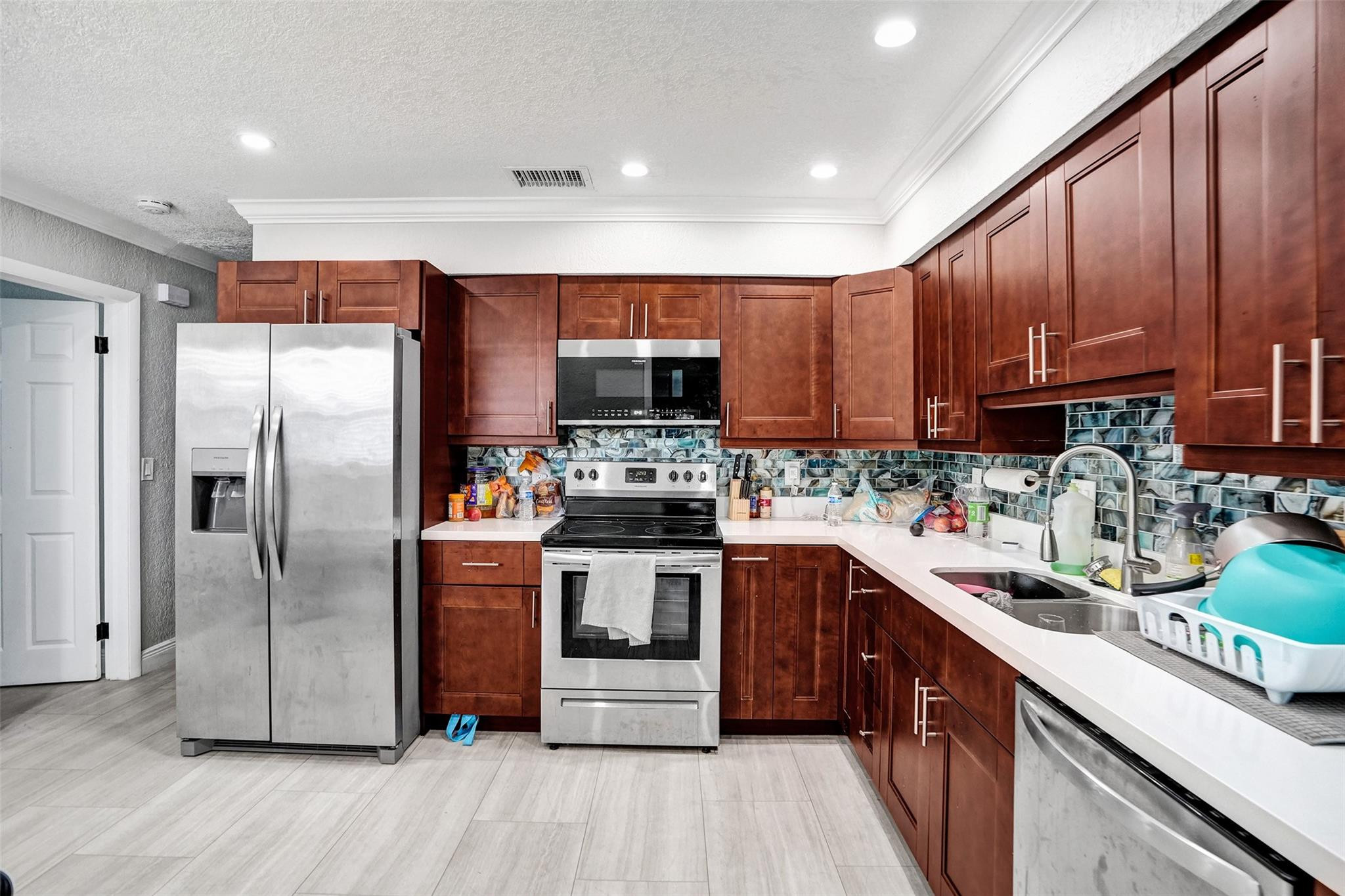 Kitchen with reddish-brown cabinets, stainless appliances, and a blue-gray mosaic backsplash.