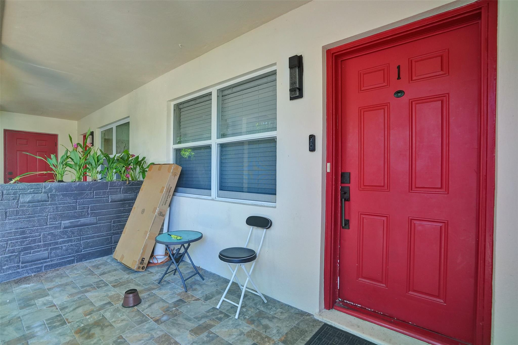 Covered entry with a bright red front door, large window, tiled floor, and raised planter.