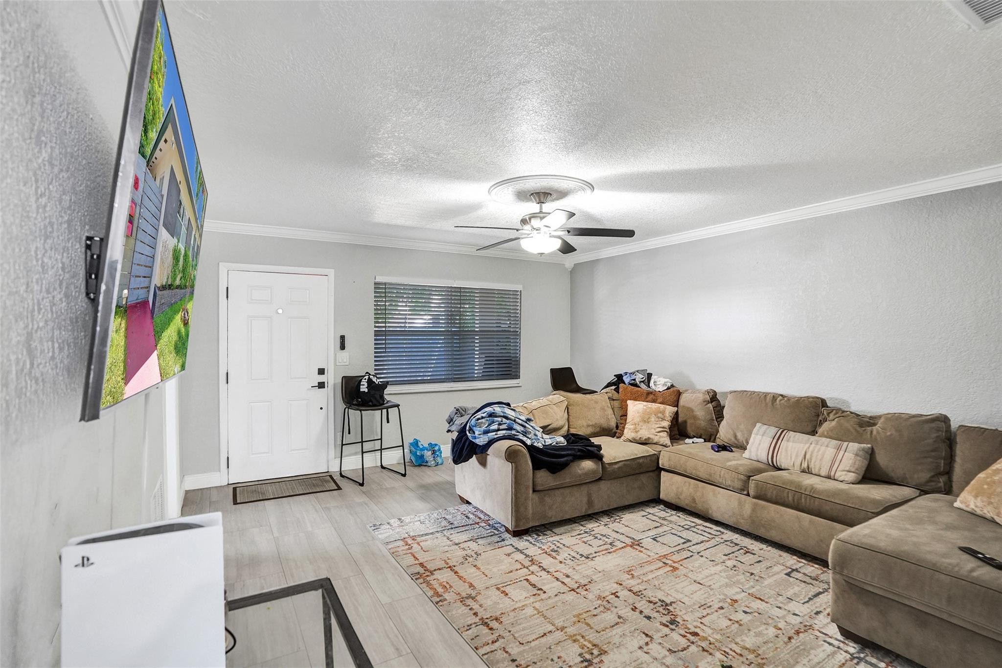 Living room with a beige sectional, patterned rug, ceiling fan, and wall-mounted television.