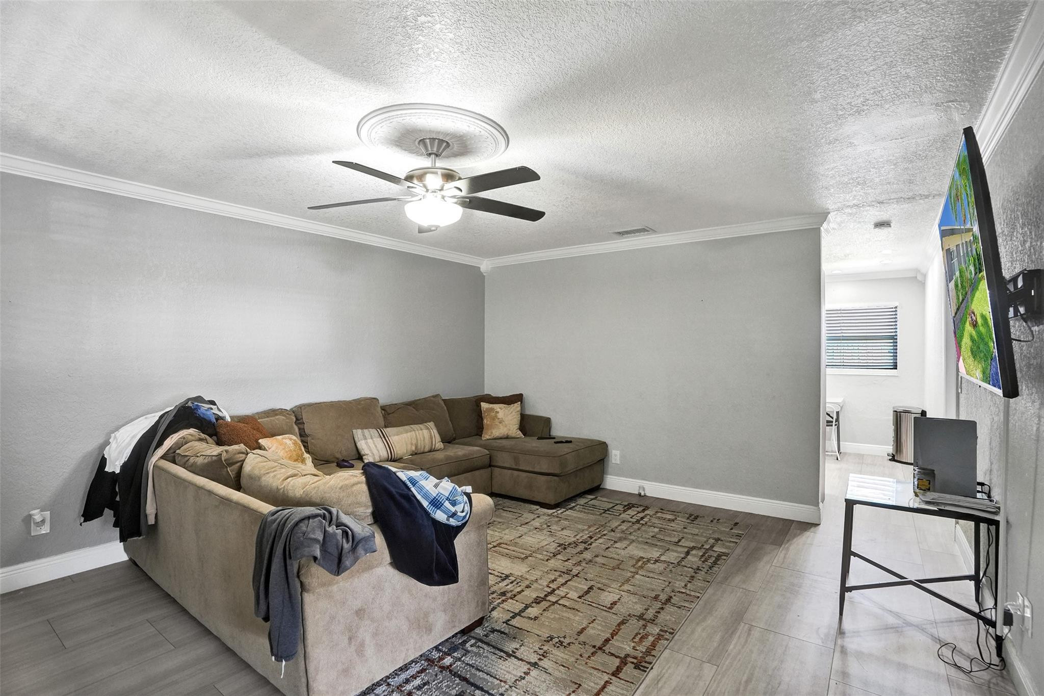 Living room with a large sectional sofa, patterned rug, ceiling fan, and wall-mounted television.