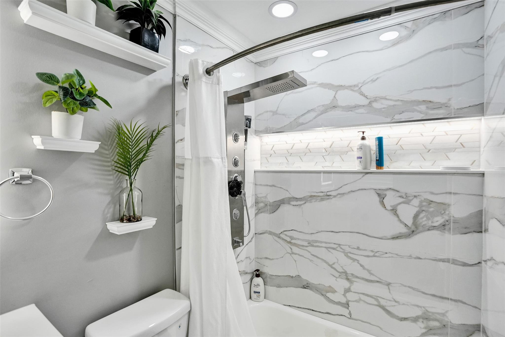 Bathroom with a marble-tiled tub shower, glass screen, and rainfall showerhead.