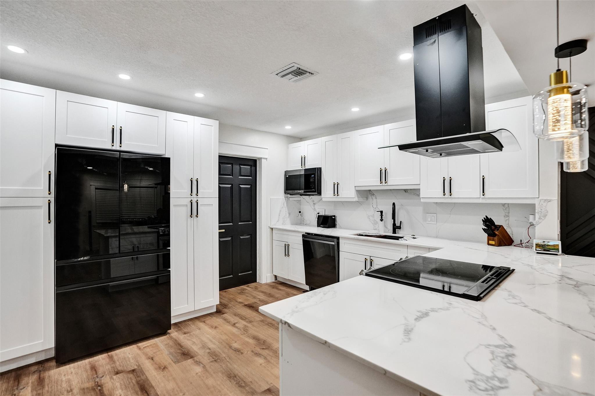 Kitchen with white cabinetry, black appliances, marble-look island, and wood flooring.