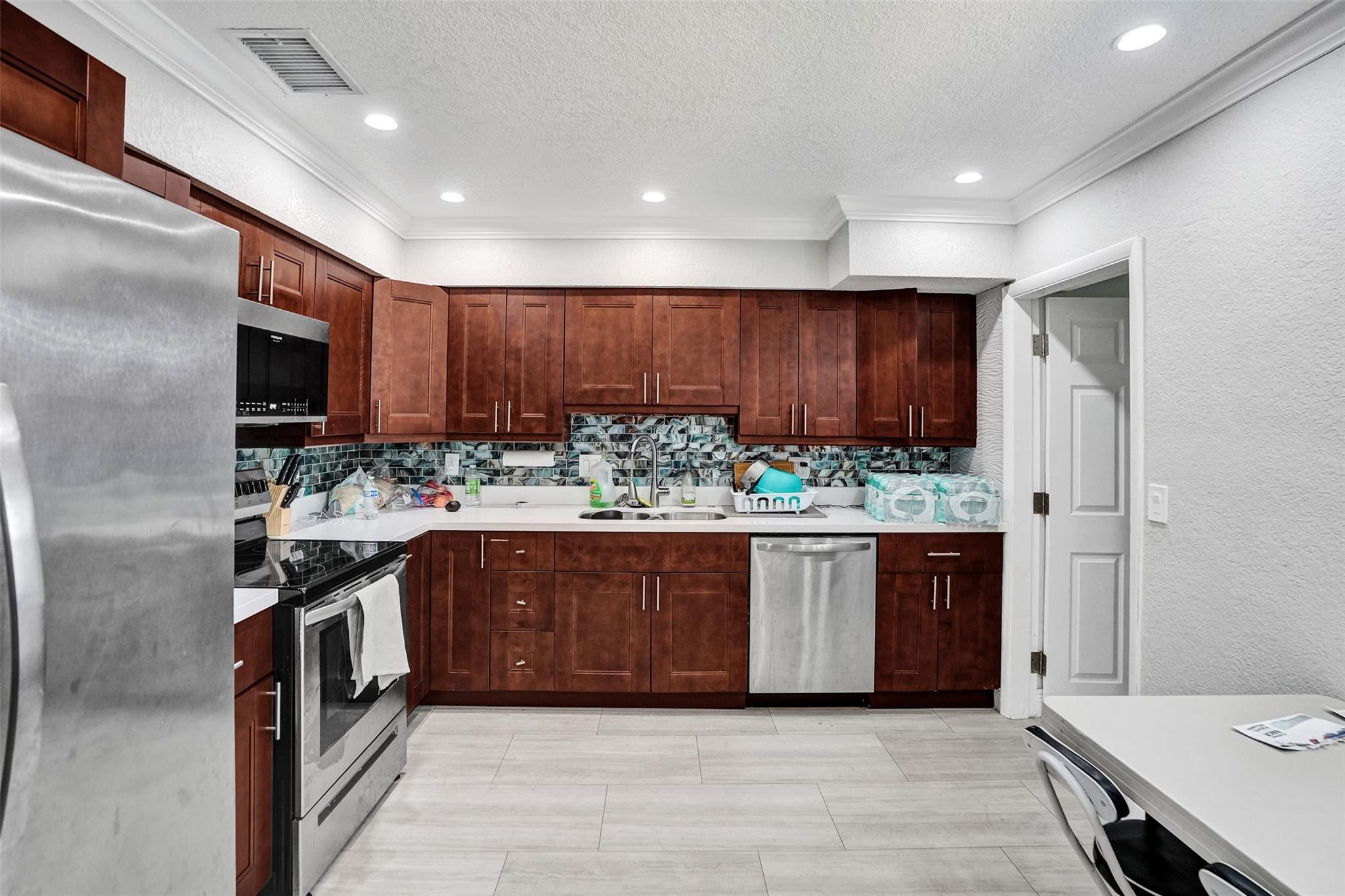 Kitchen with dark wood cabinets, mosaic tile backsplash, and stainless steel appliances.