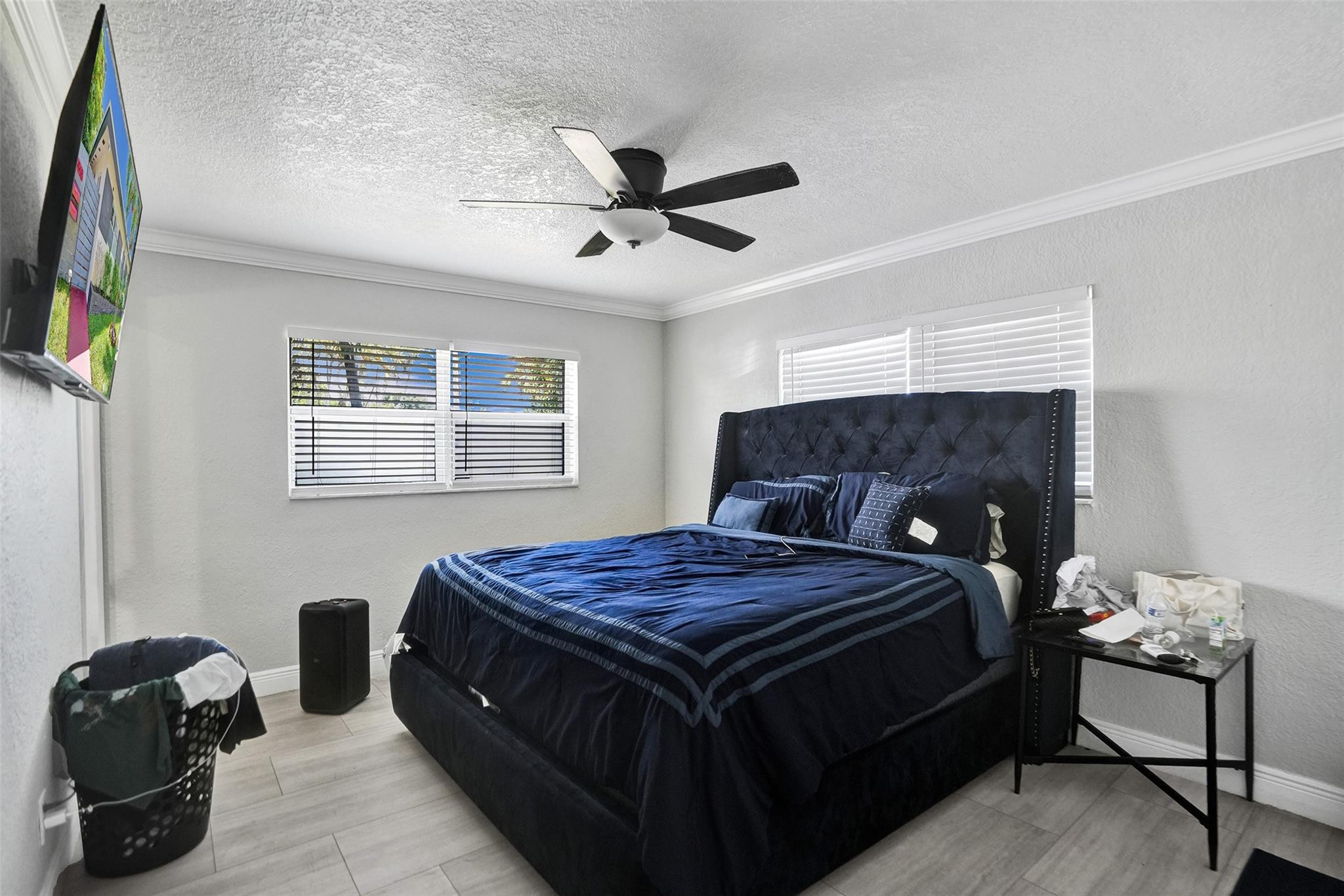 Bedroom with a large dark blue bed, tufted headboard, ceiling fan, and windows with blinds.