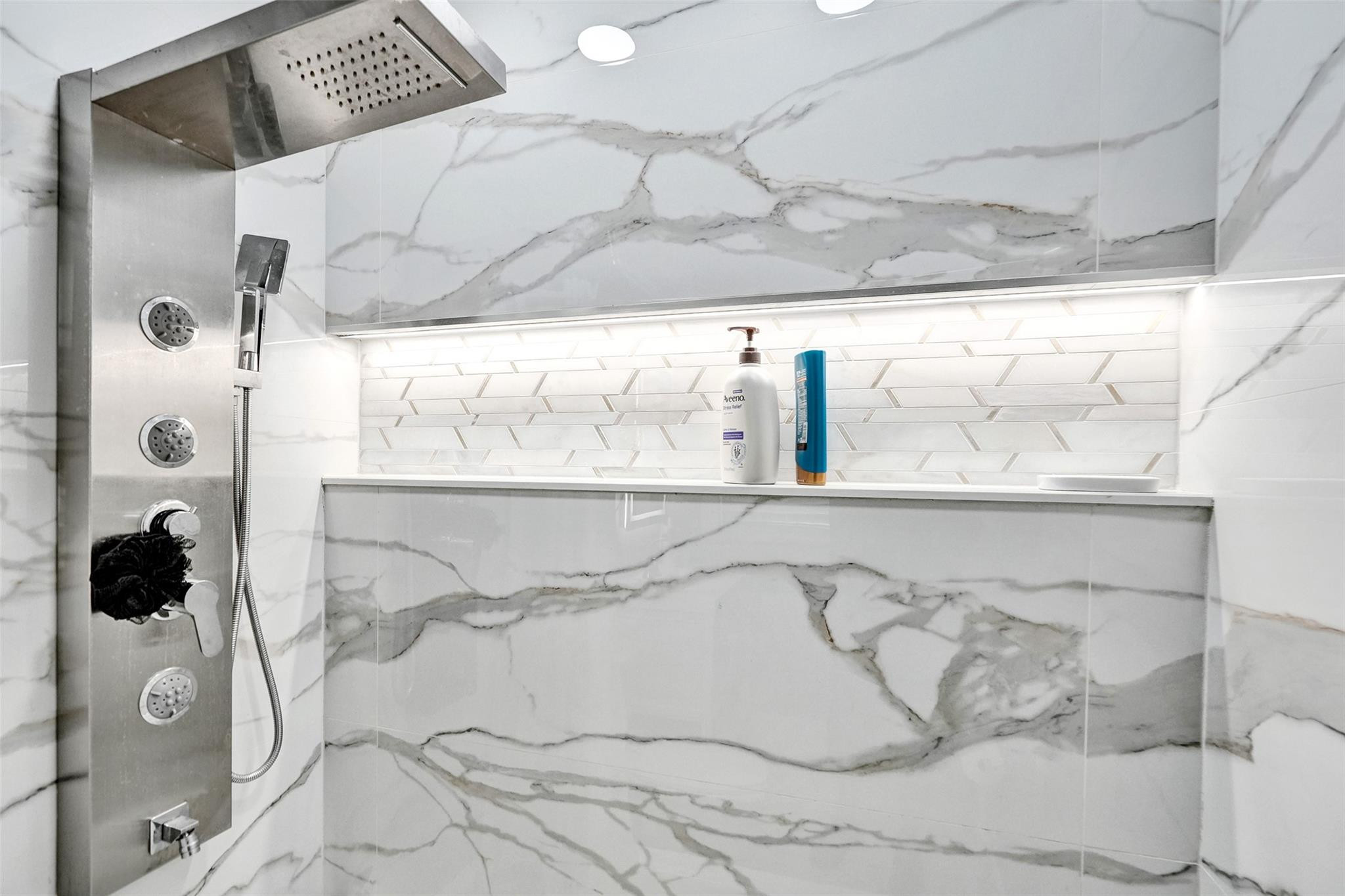 Modern marble-look shower with multiple body sprays and a recessed shelf.