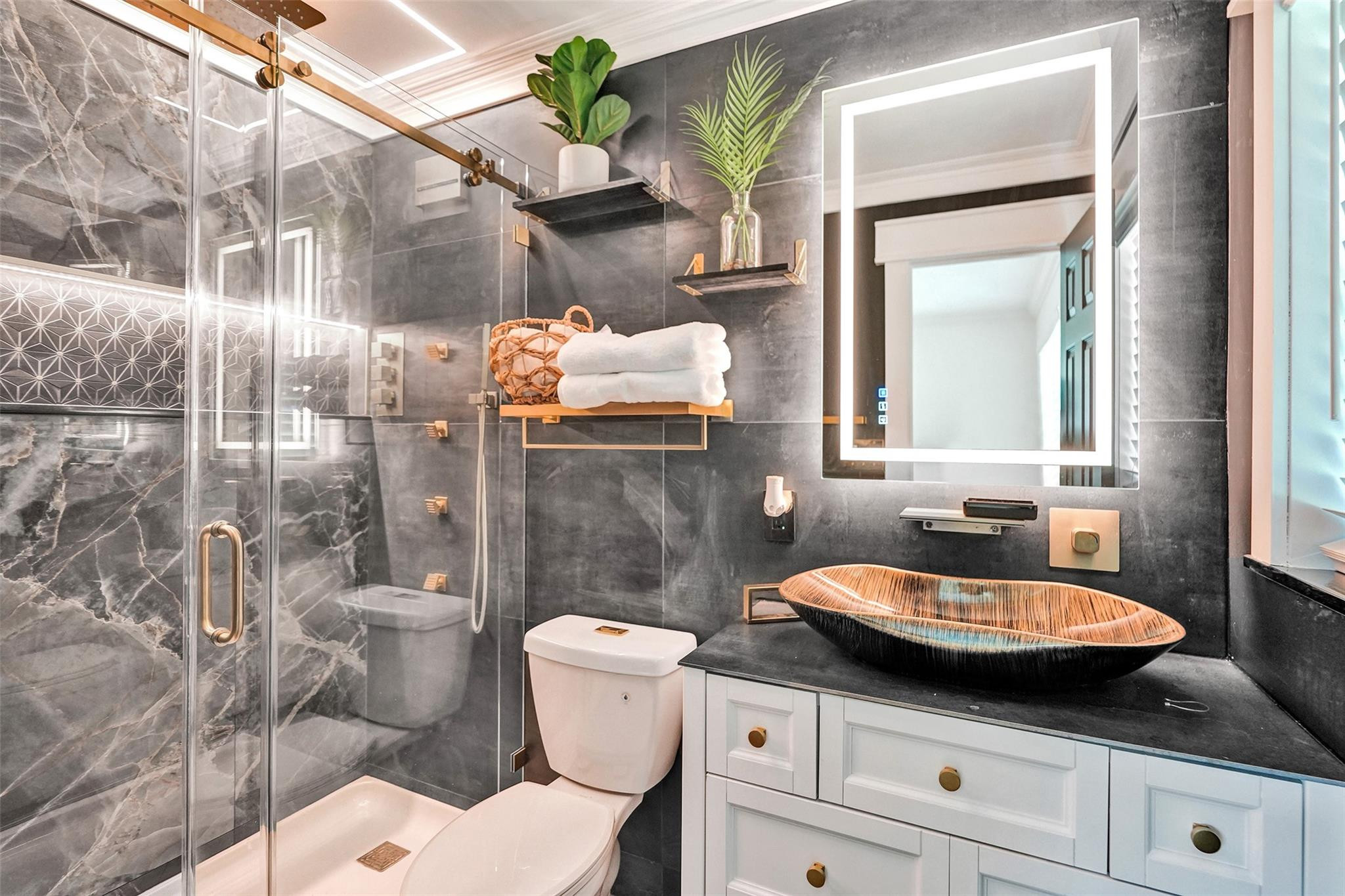 Modern bathroom with a glass shower, dark marble walls, and a wood-toned vessel sink.