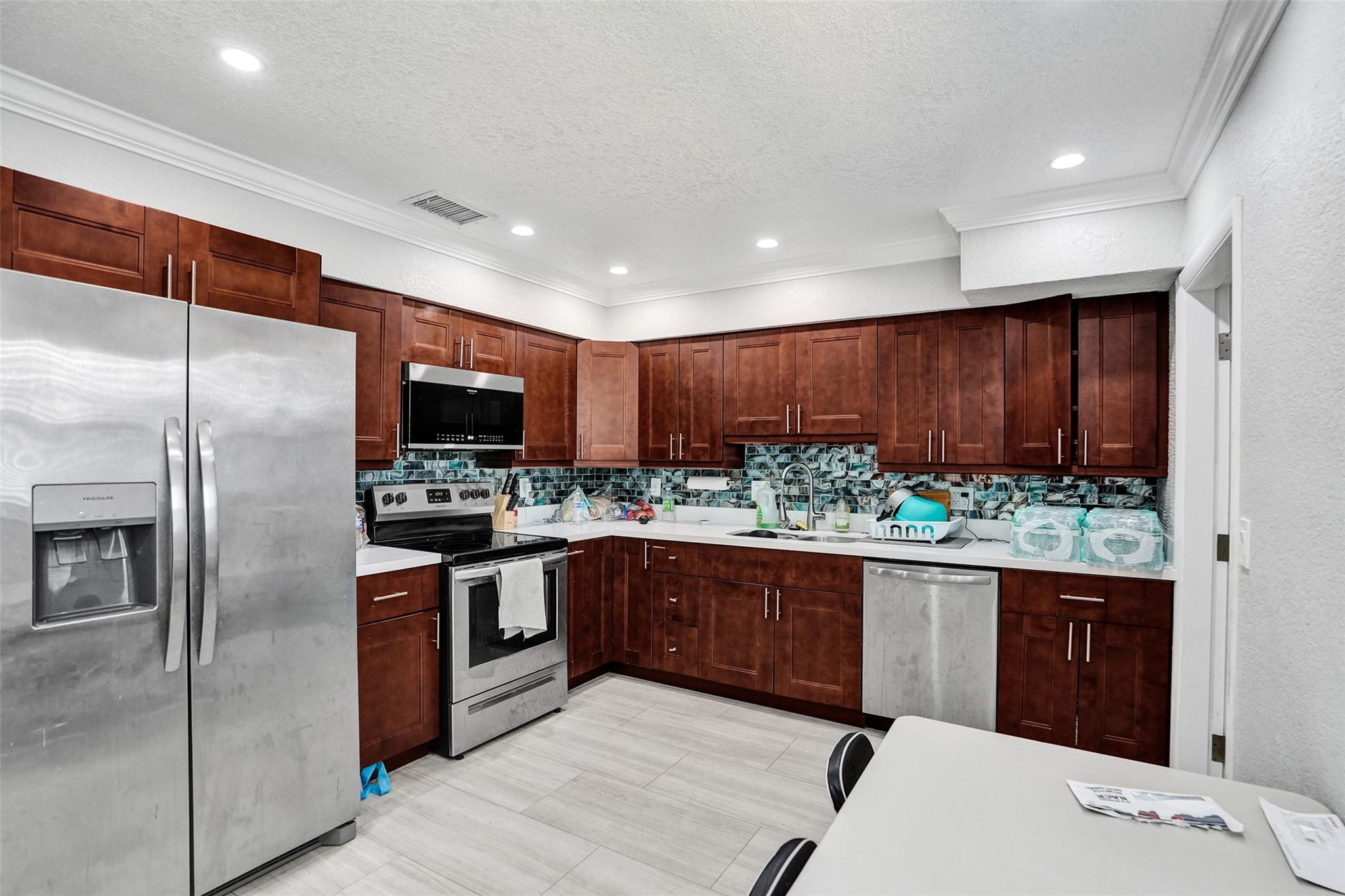 Kitchen with dark wood cabinets, stainless appliances, and a blue-green mosaic backsplash.