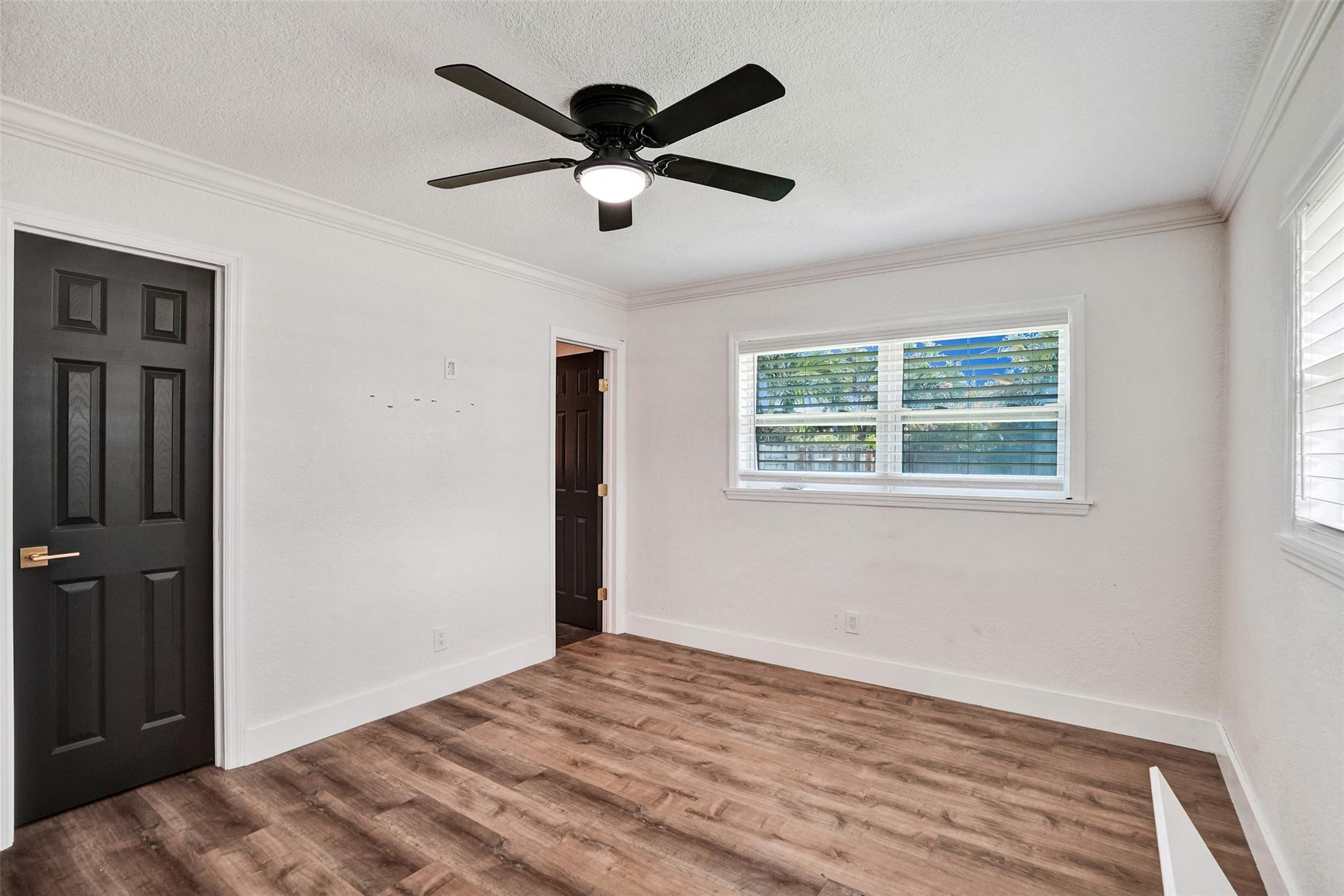 Unfurnished bedroom with wood-look flooring, a black ceiling fan, and a window with blinds.