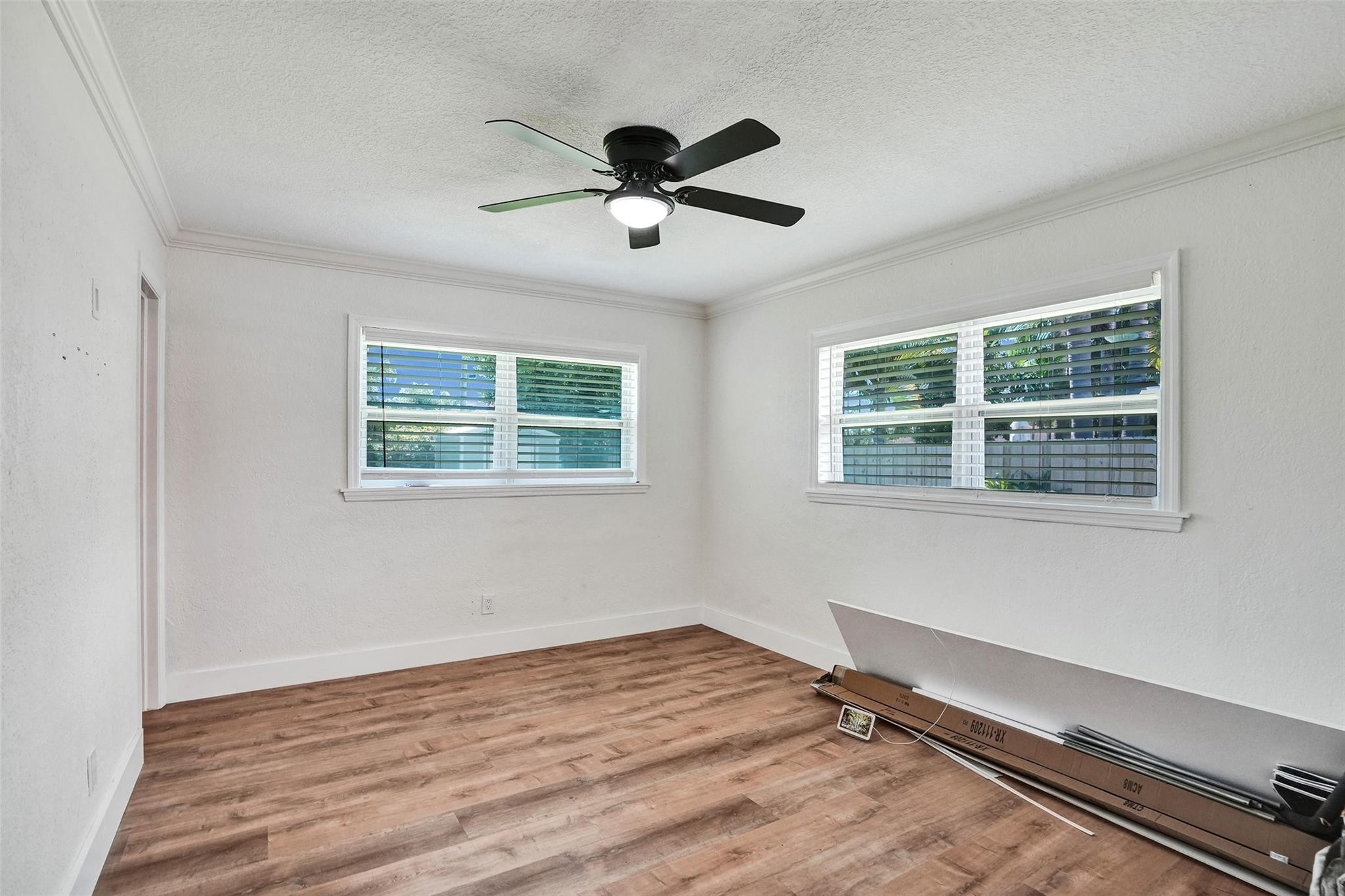 Empty room with wood-look flooring, two shuttered windows, and a black ceiling fan.
