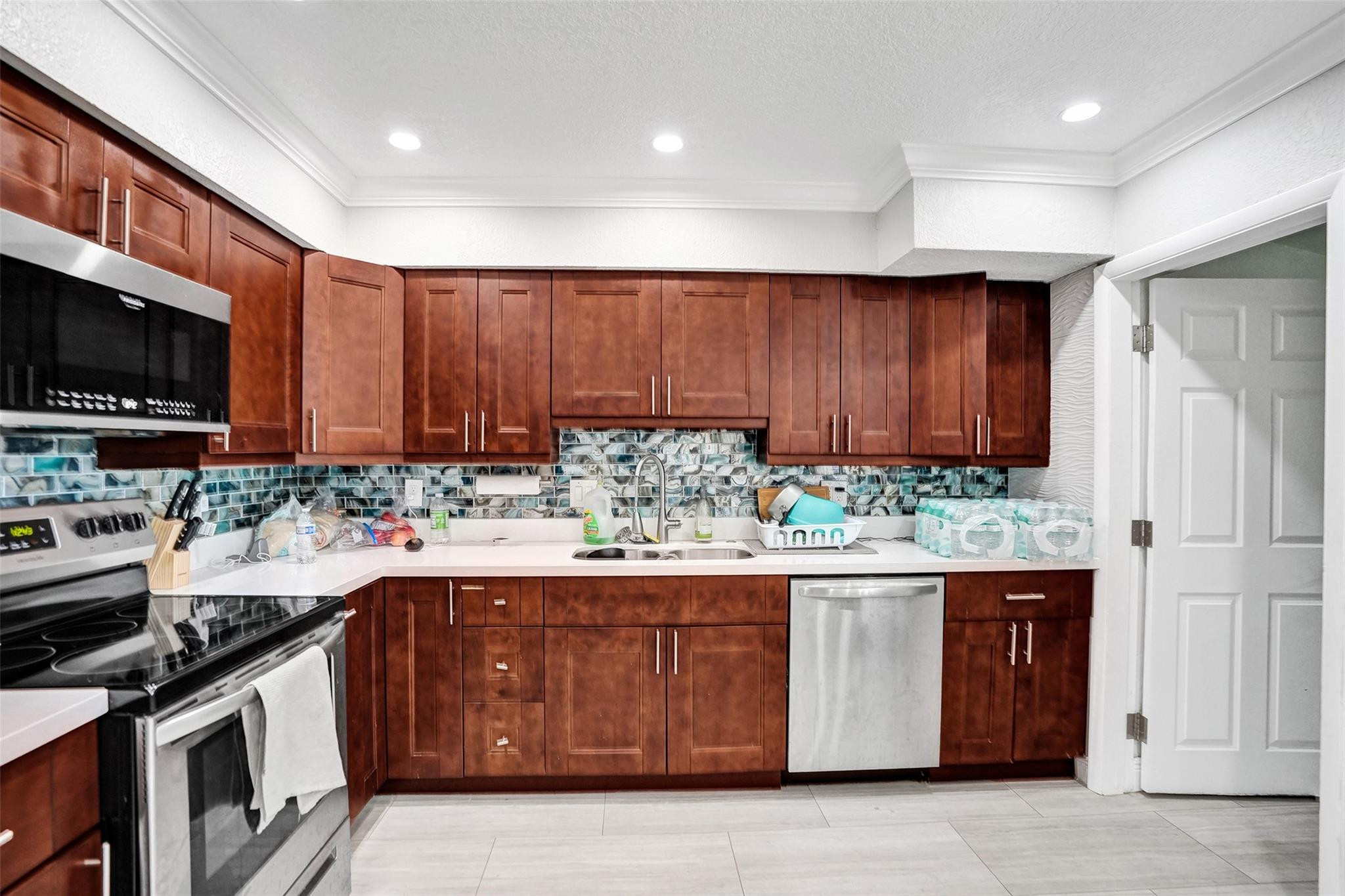 Kitchen with reddish-brown cabinets, blue-gray mosaic backsplash, and stainless steel appliances.
