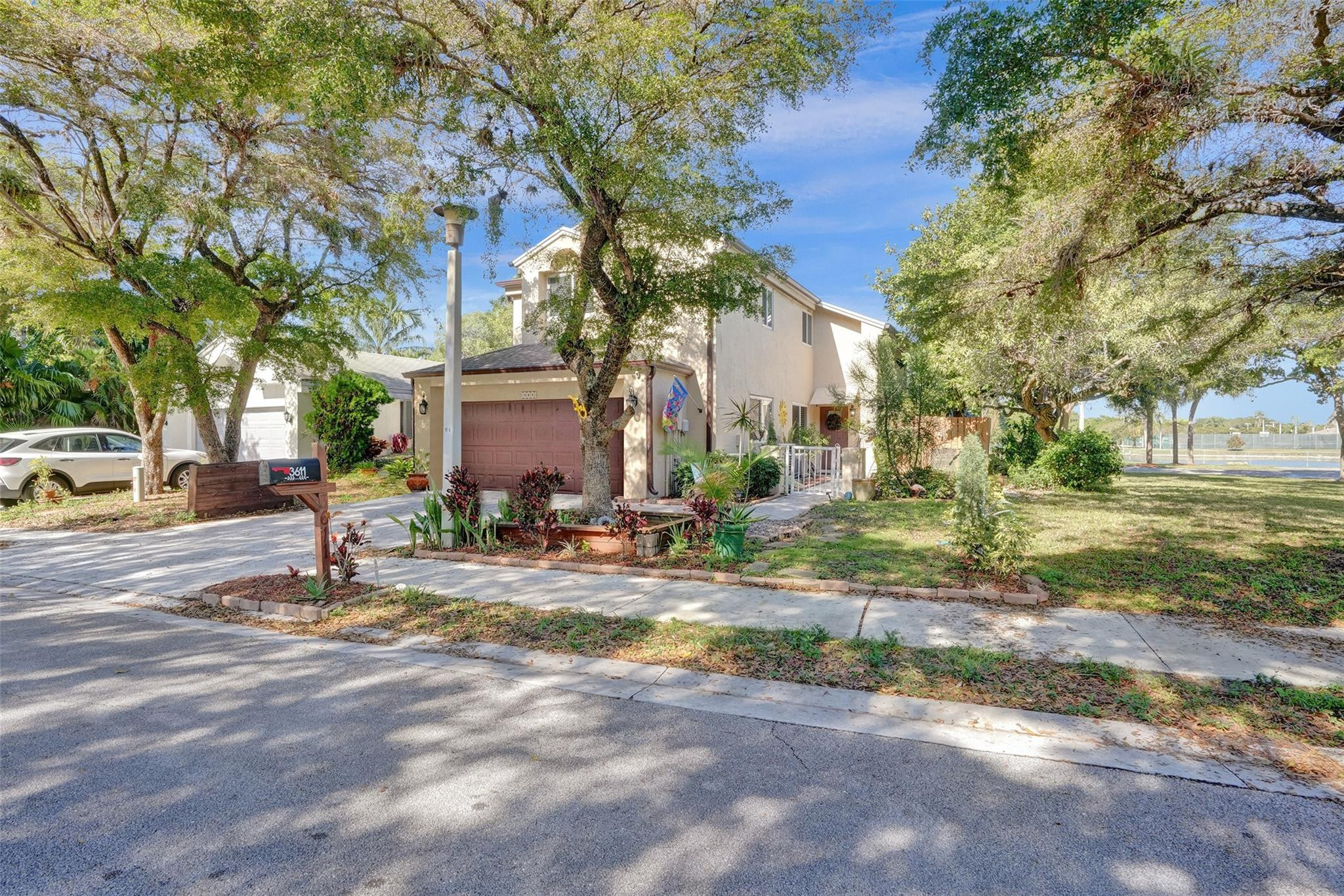 Two-story stucco home with an attached garage, mature shade trees, and a landscaped front yard.