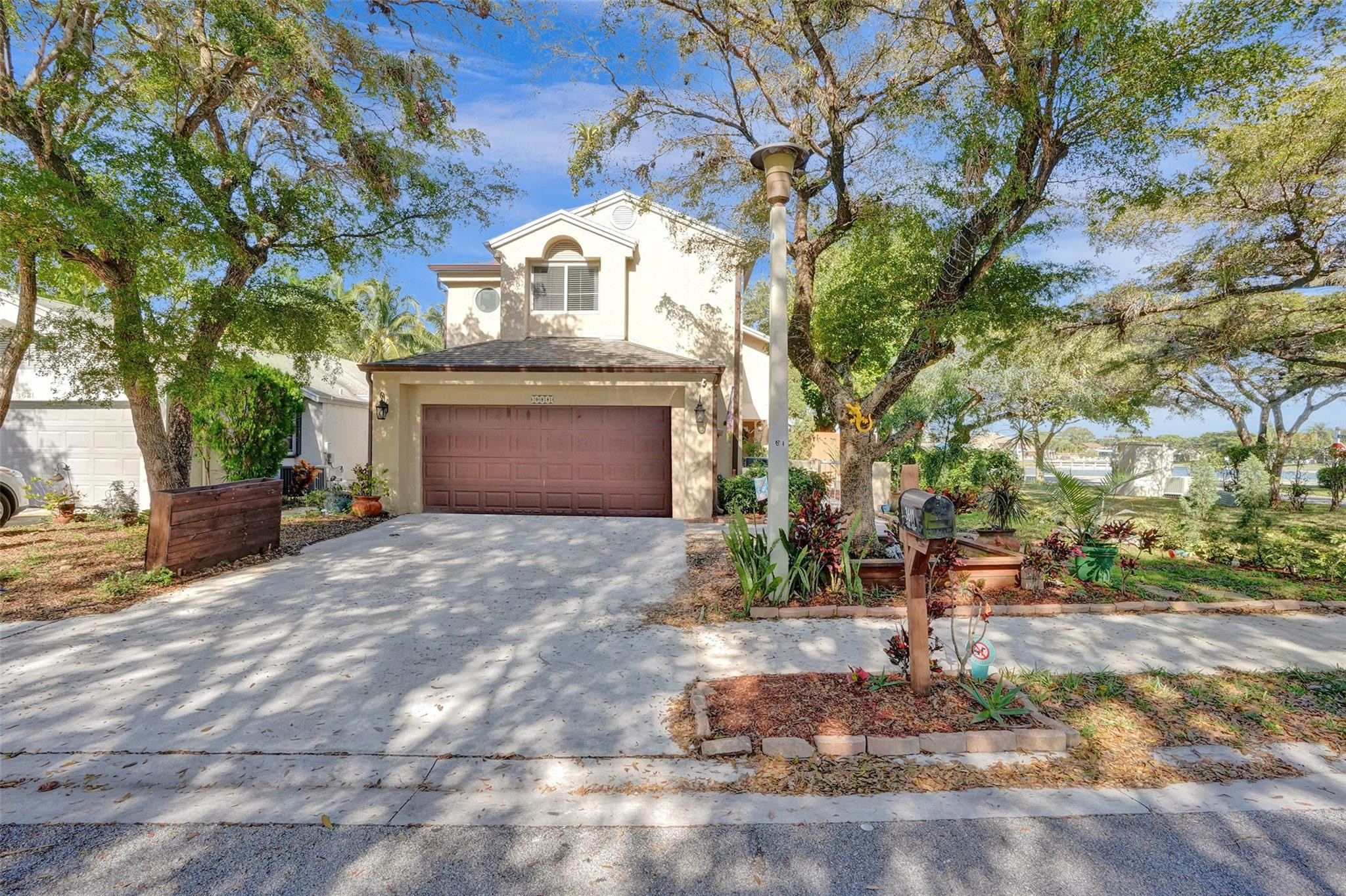 Two-story home with a double garage, shaded driveway, mature trees, and water visible beyond the yard.