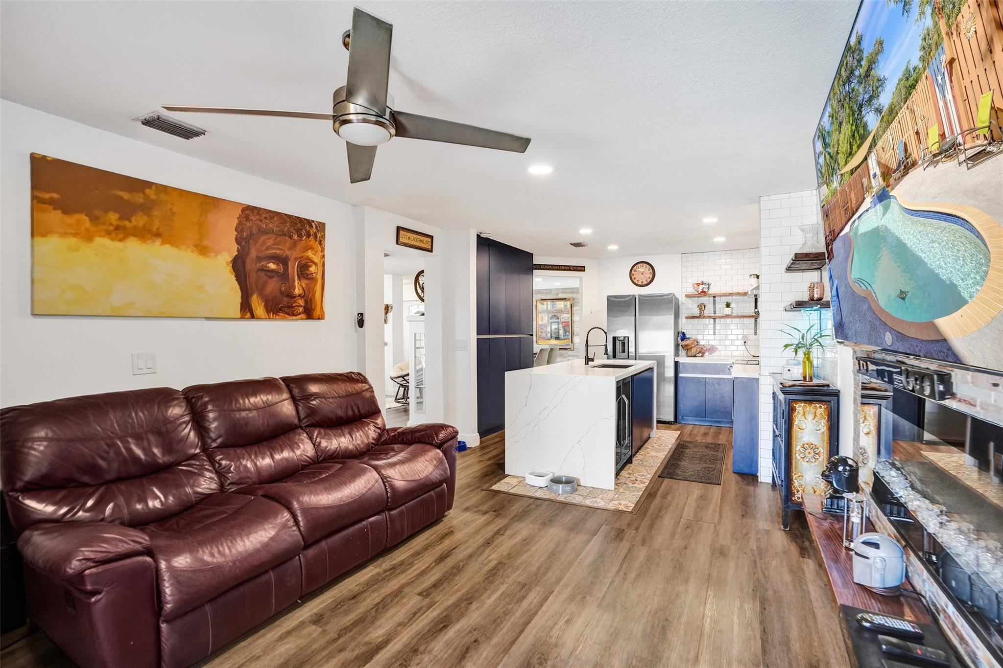 Open-plan living room and kitchen with a burgundy leather sectional and white island.