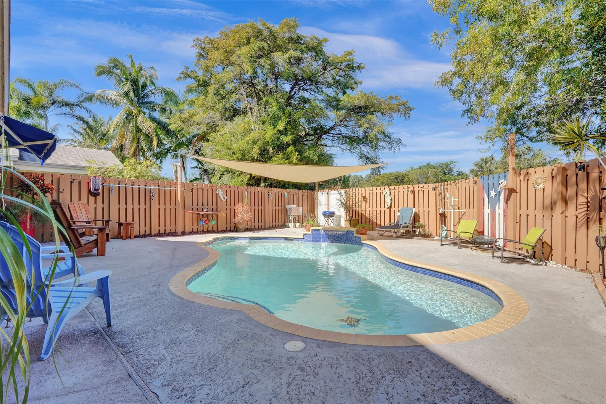 Backyard pool with a curved shape, lounge chairs, and a shade sail.