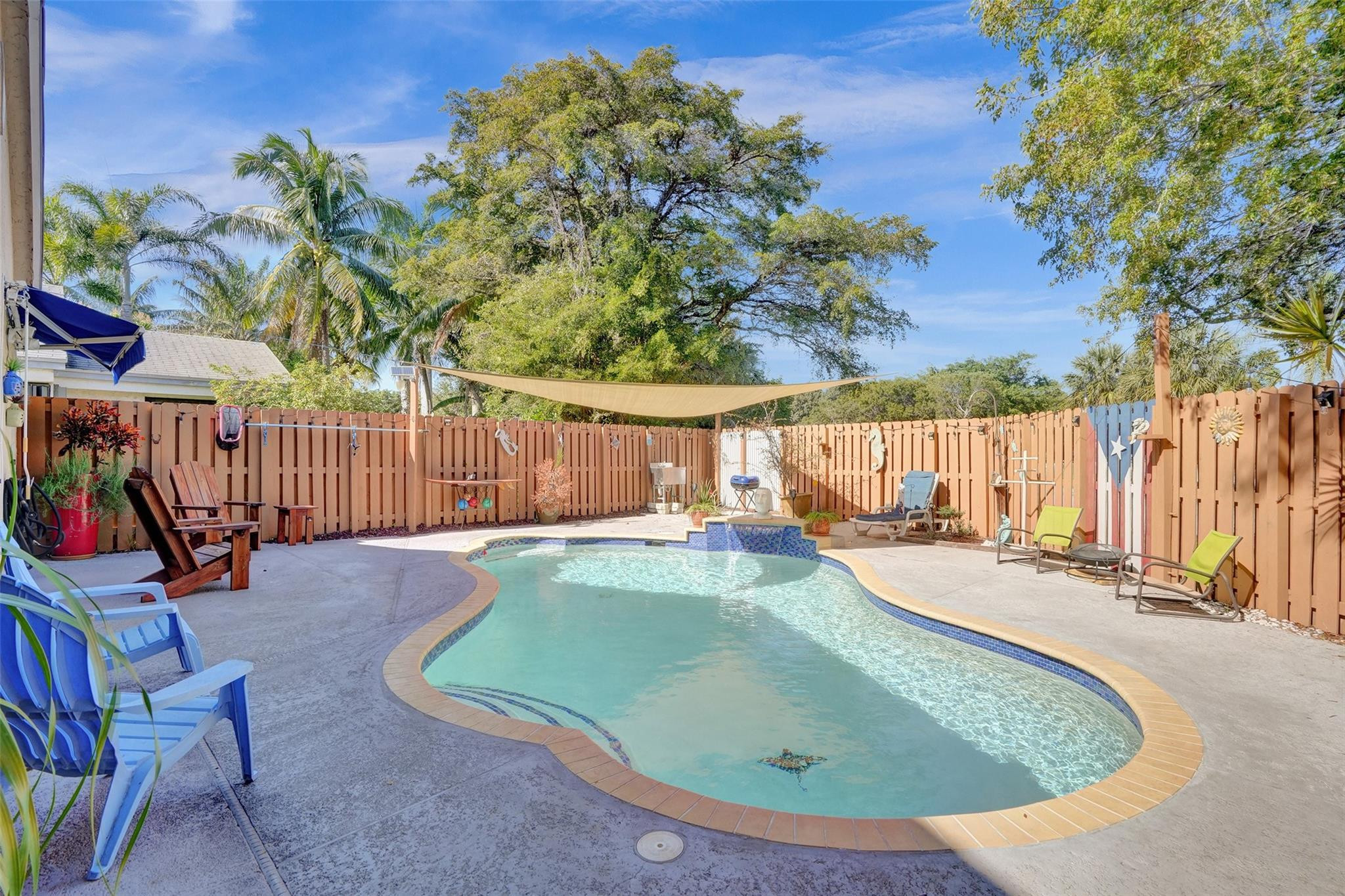 Curved backyard pool with blue tile accents, a shade sail, and lounge chairs on the patio.