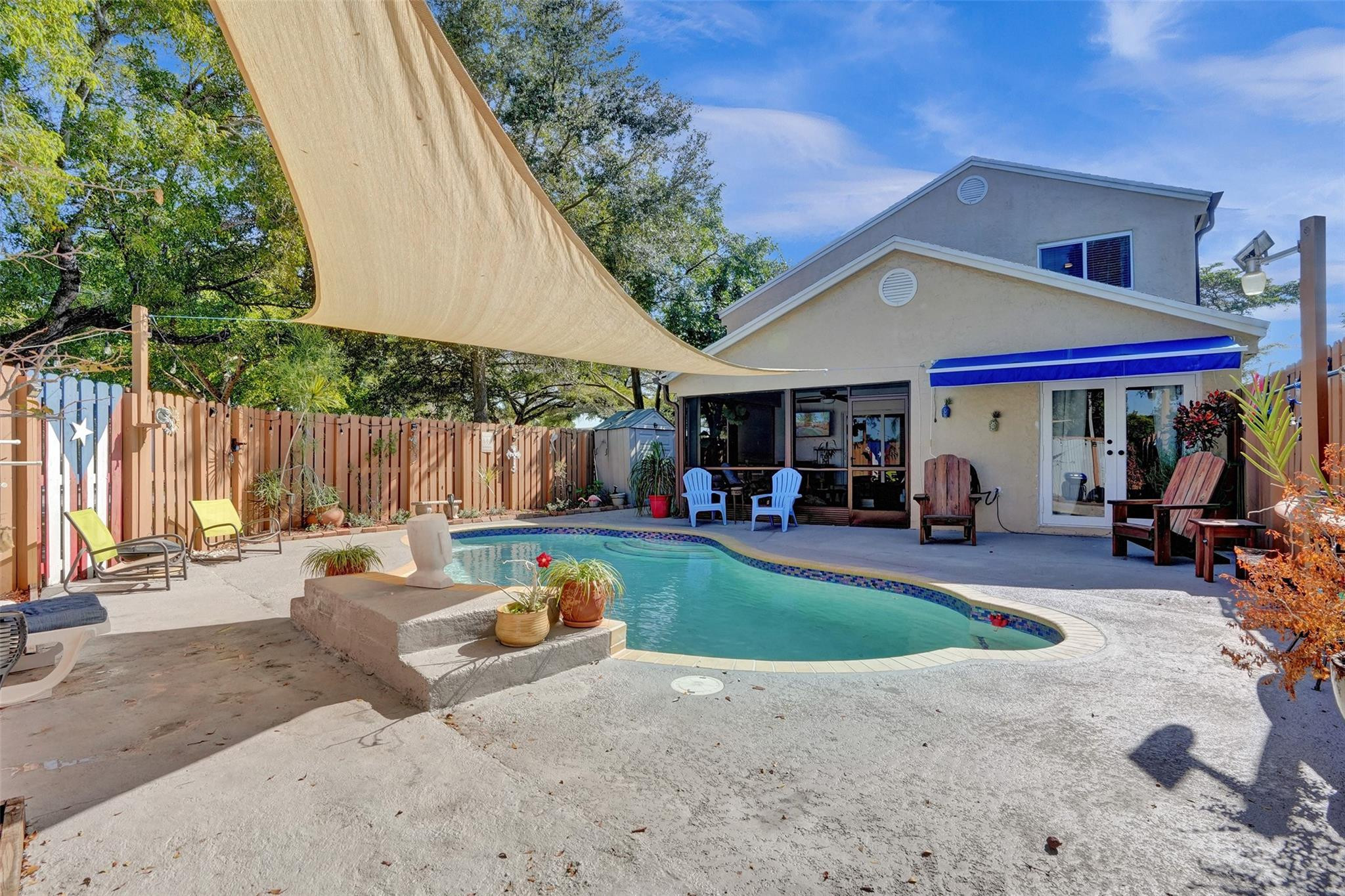 Backyard pool beside the house, shaded by a tan sail with a blue awning over the patio.