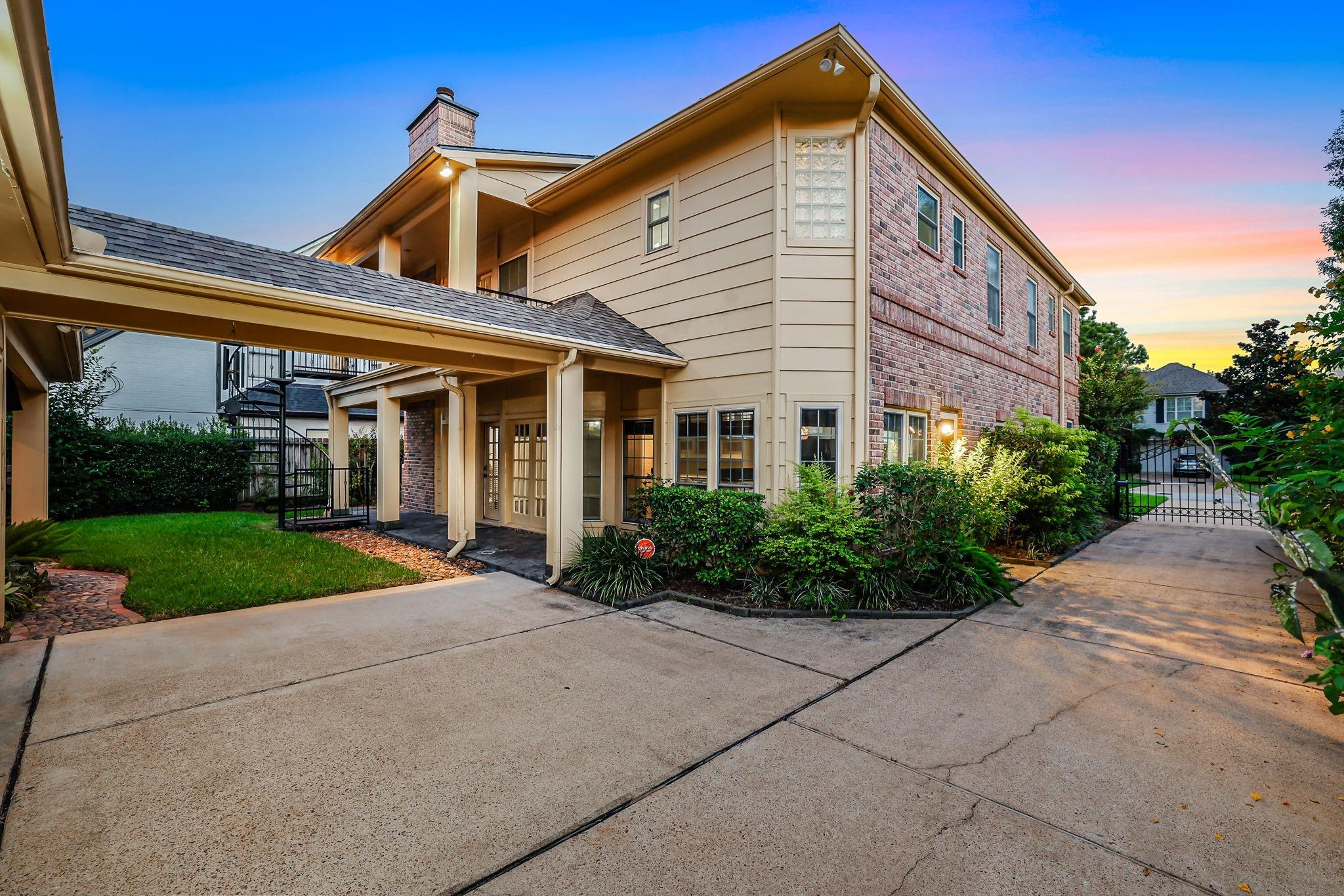 Two-story brick-and-siding home with a covered patio and landscaped driveway at dusk.