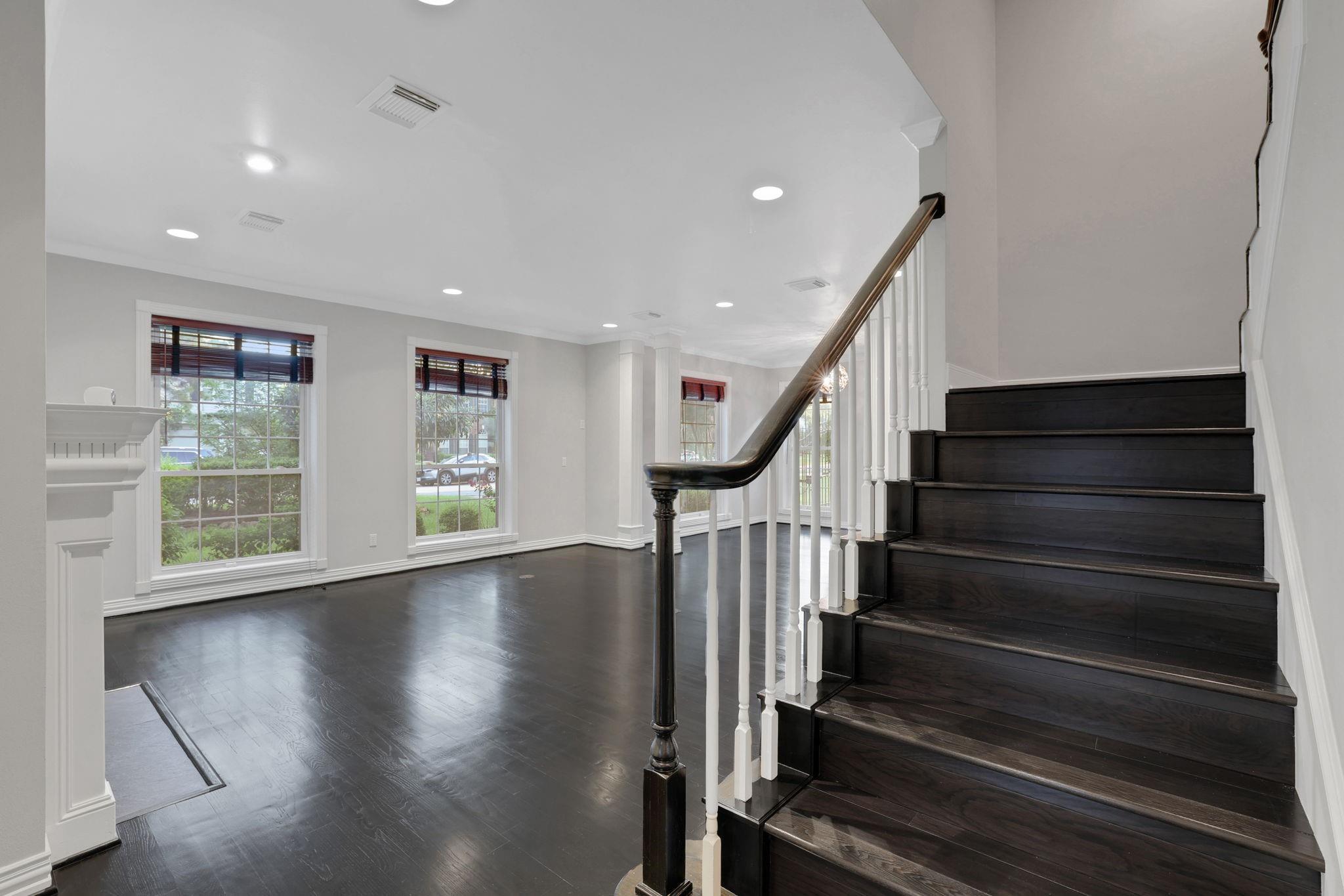 Empty foyer with a dark hardwood staircase, white balusters, tall windows, and dark wood floors.