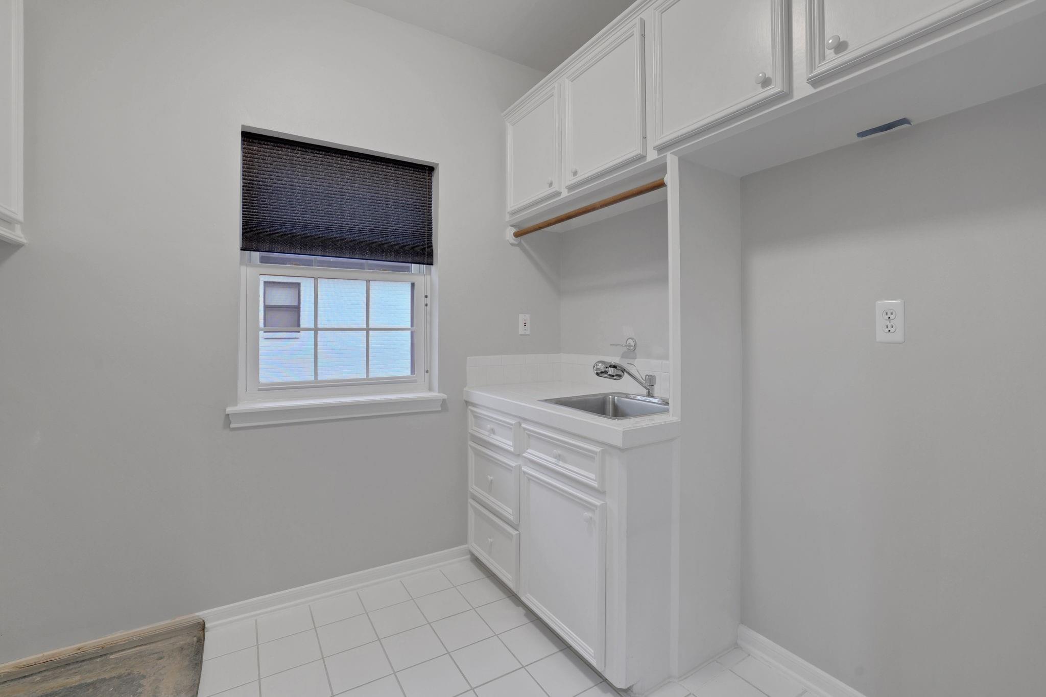 Laundry room with white built-in cabinets, a utility sink, hanging rod, and shaded window.