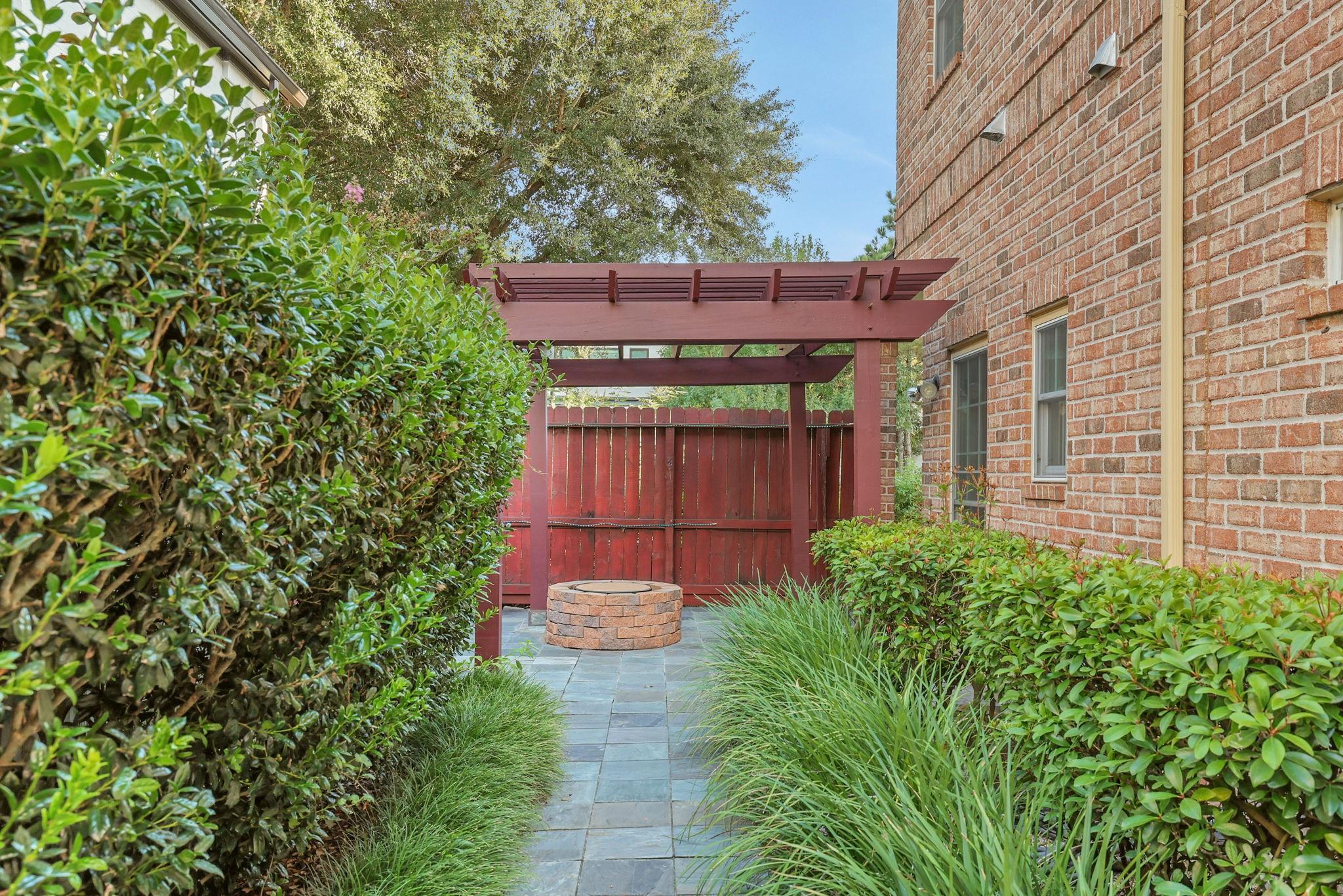 Brick home's landscaped side patio with a red pergola, slate walkway, and circular stone fire pit.