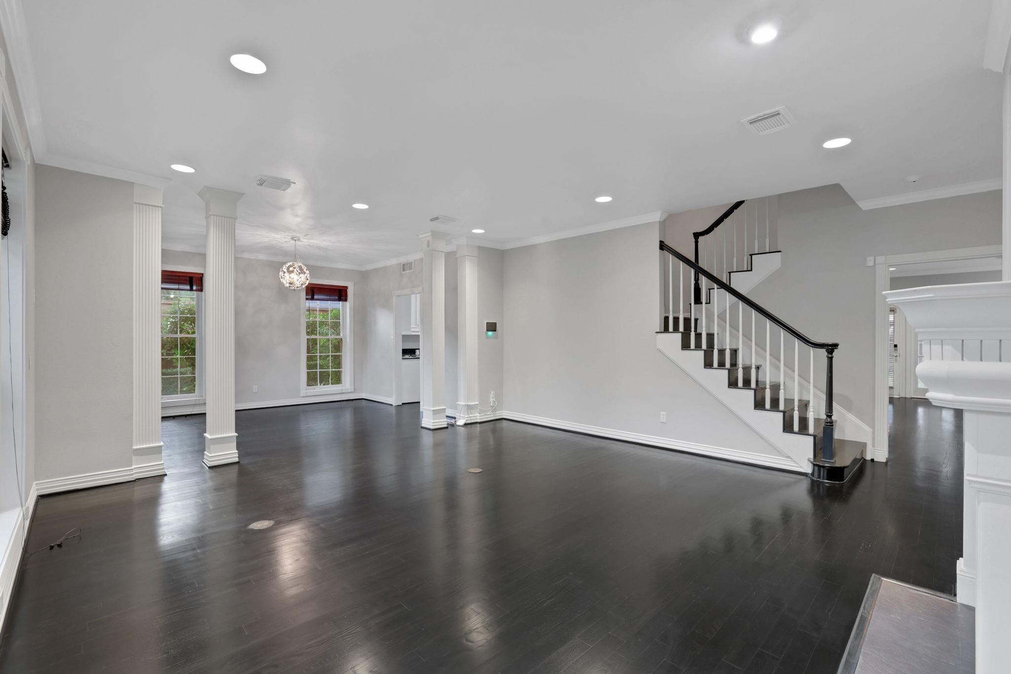 Empty living area with dark hardwood floors, white columns, and a staircase with dark railing.