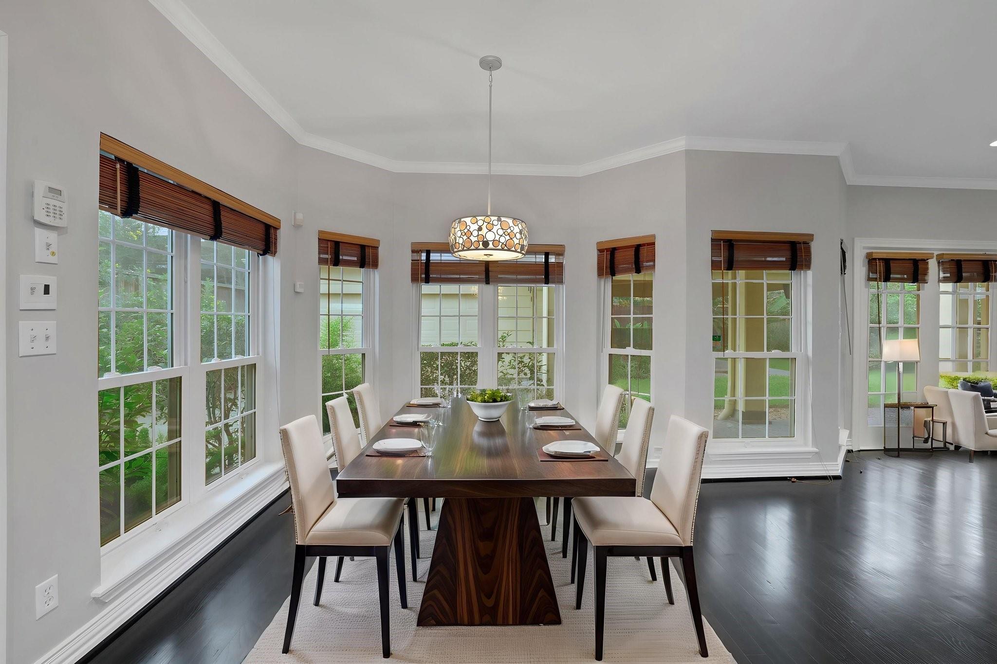 Dining room with a dark wood table, cream chairs, large windows, and a patterned pendant light.