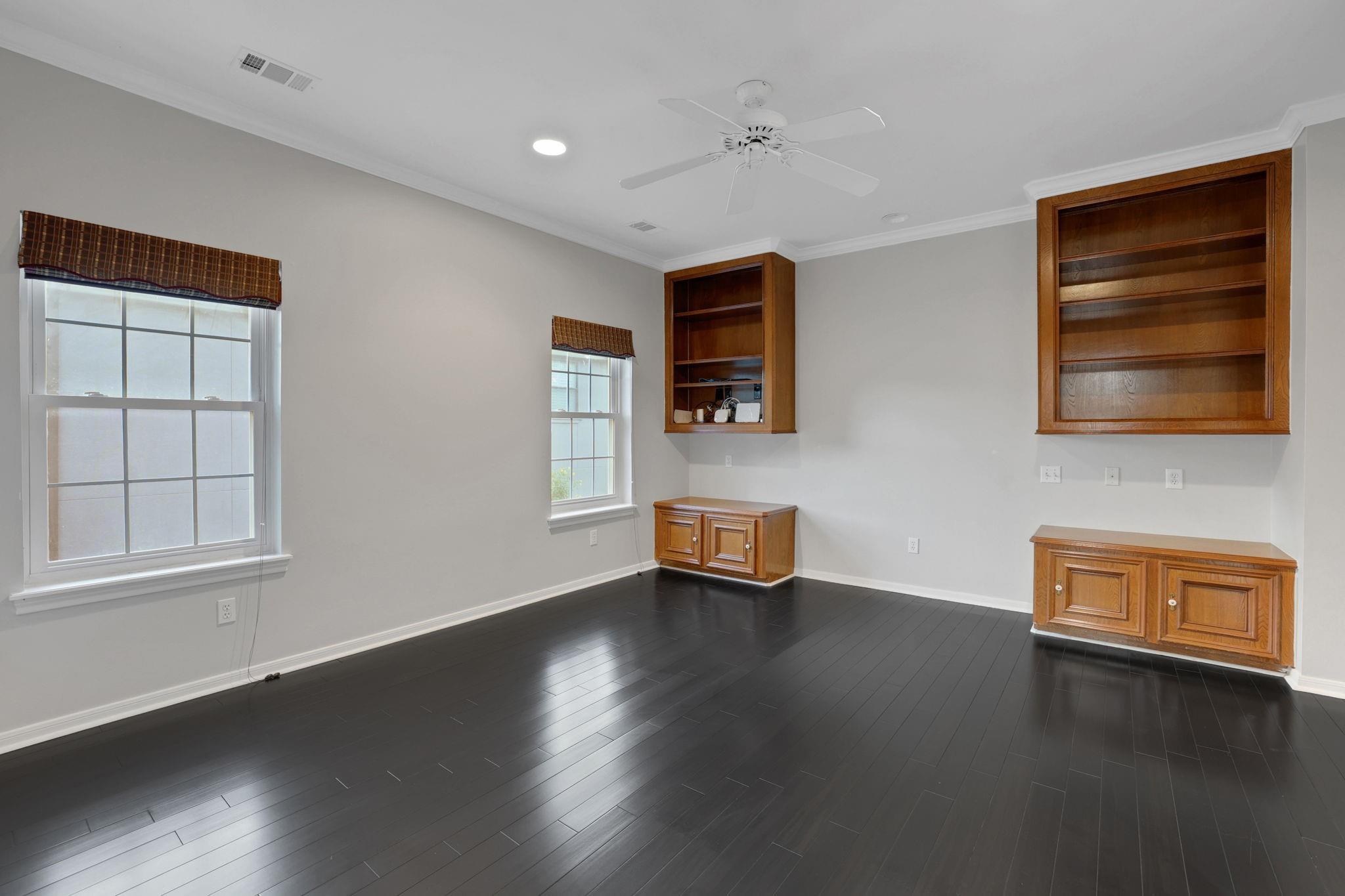 Empty room with dark hardwood floors, built-in wood shelving and cabinets, and two windows.
