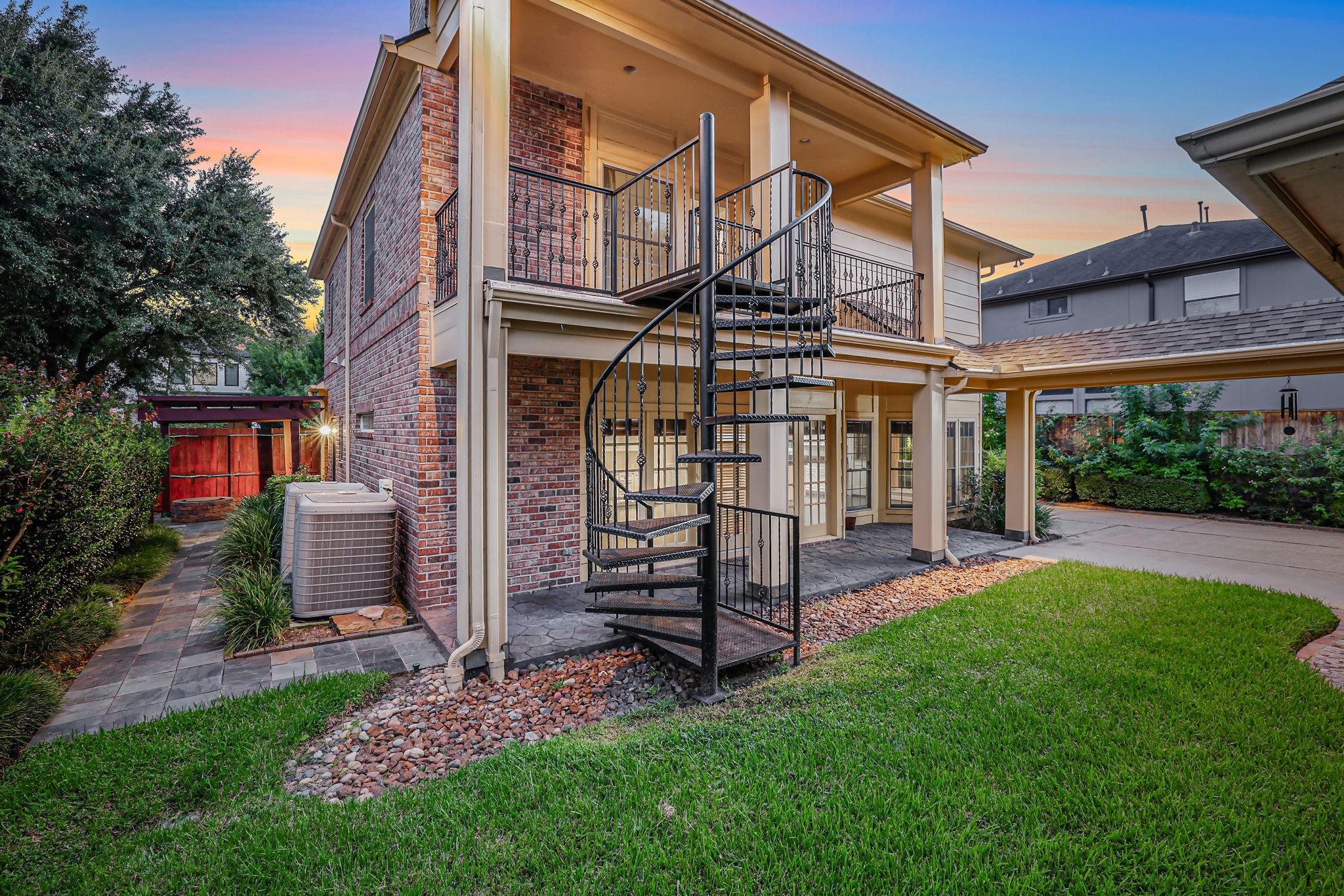 Two-story brick home with a black spiral staircase, upper balcony, and covered patio.