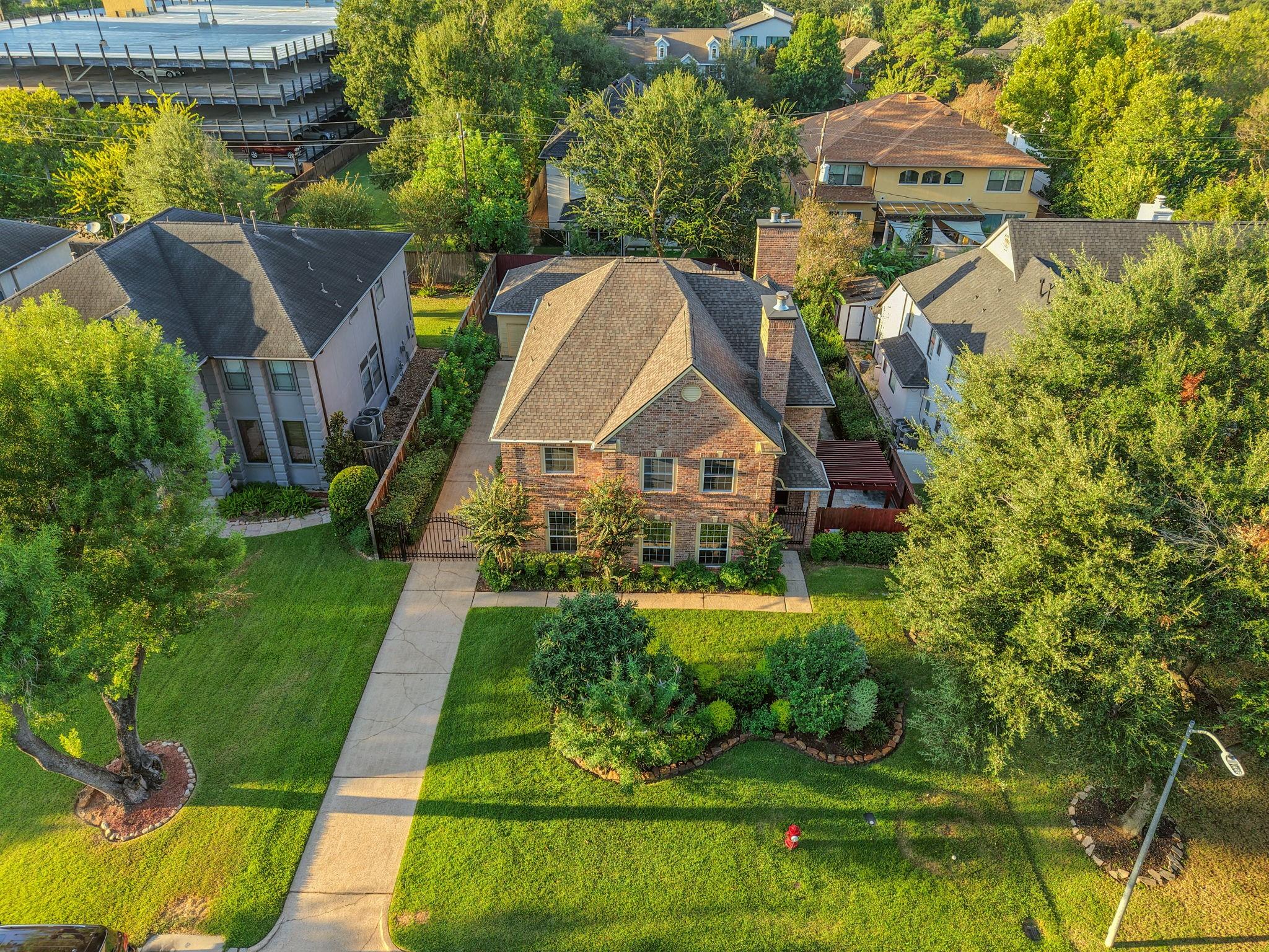 Aerial view of a two-story brick house with a landscaped lawn and concrete driveway.