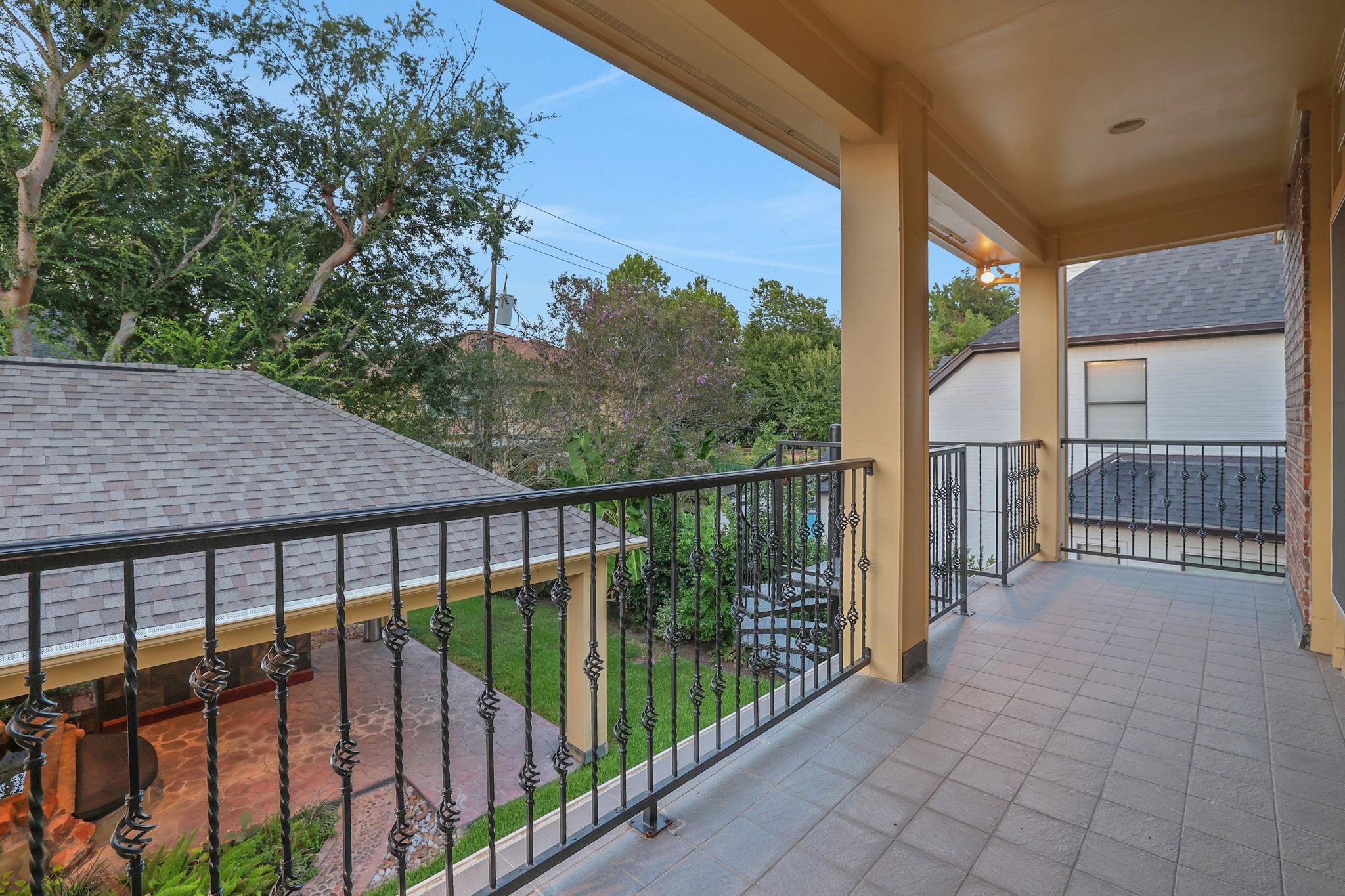 Covered tiled balcony with decorative iron railings overlooking trees and neighboring rooftops.