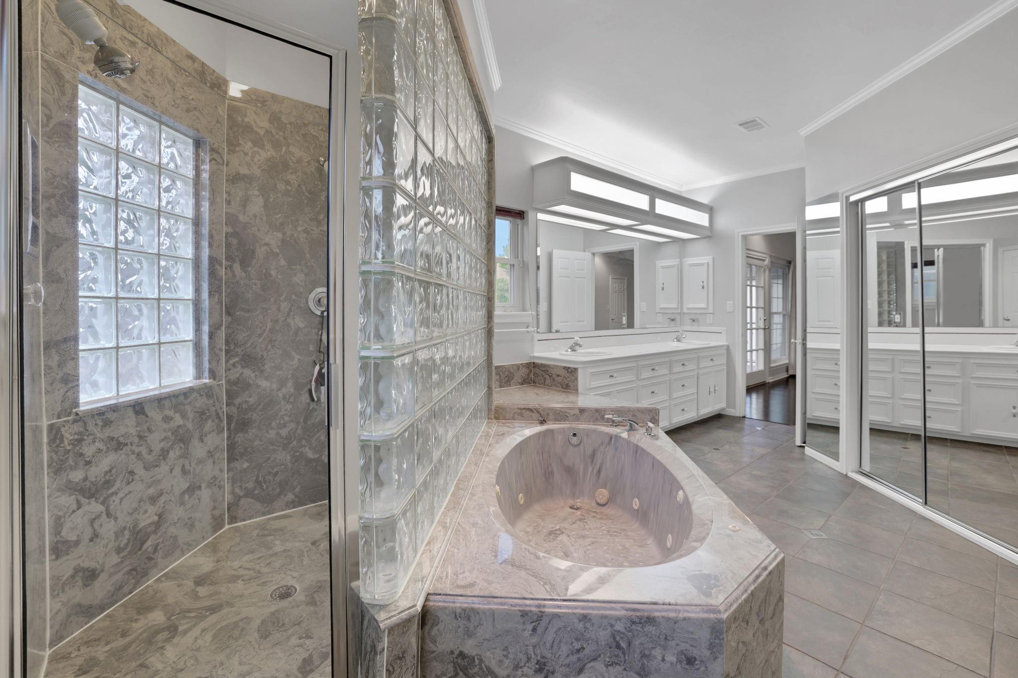 Primary bathroom with a glass-block shower, corner whirlpool tub, and white double vanity.