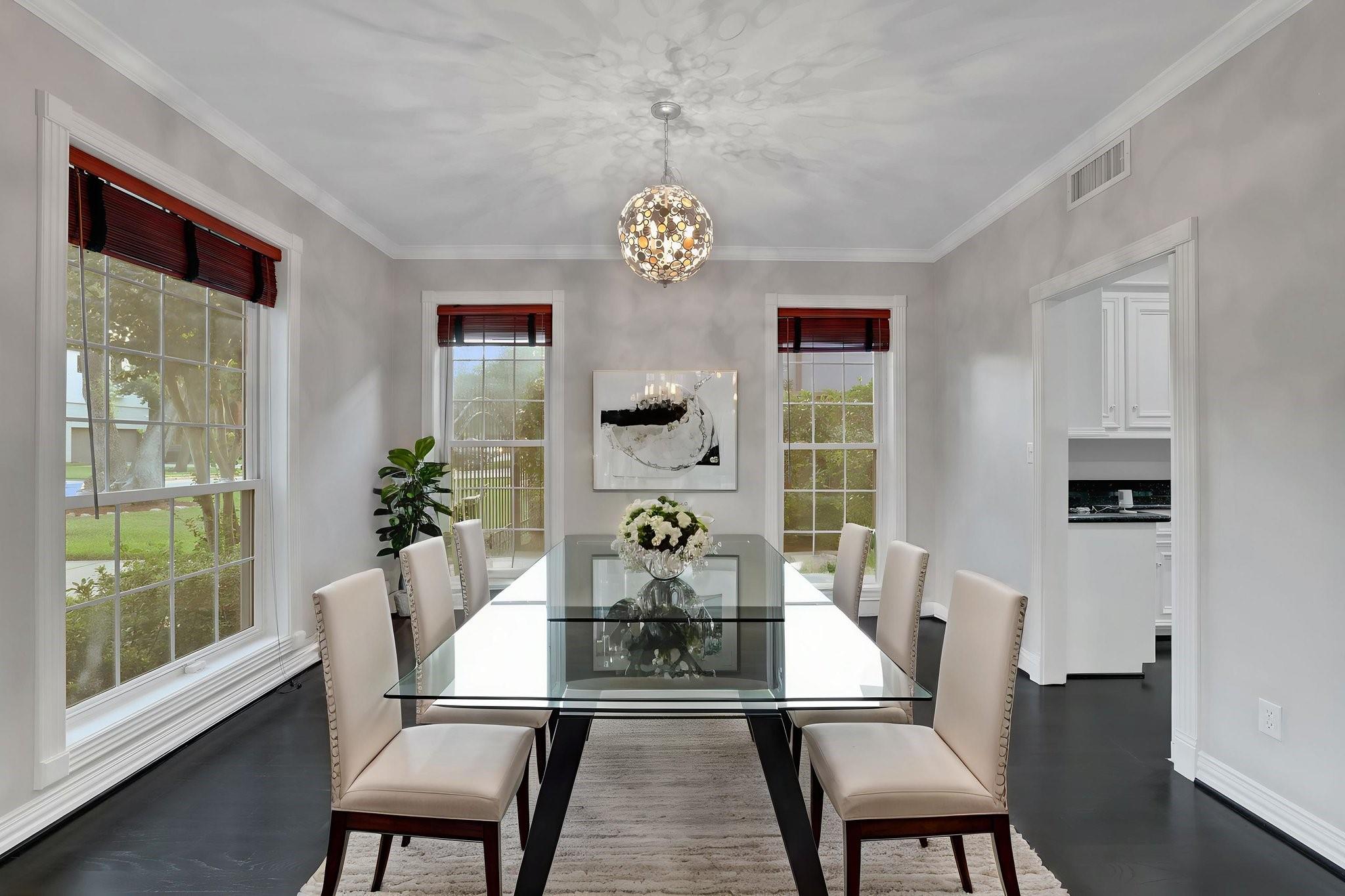 Dining room with a glass-top table, upholstered chairs, large windows, and a decorative pendant chandelier.