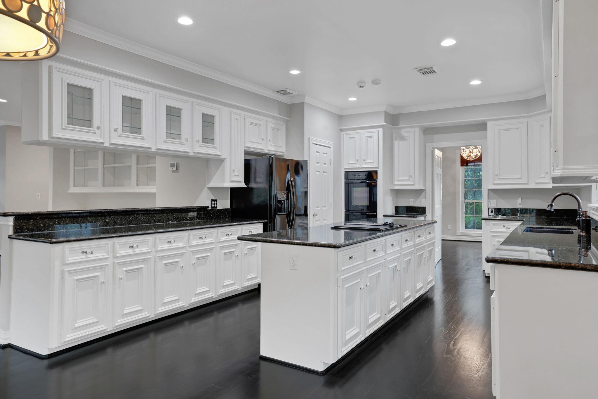 Kitchen with white paneled cabinetry, black granite counters, a large island, and dark hardwood floors.
