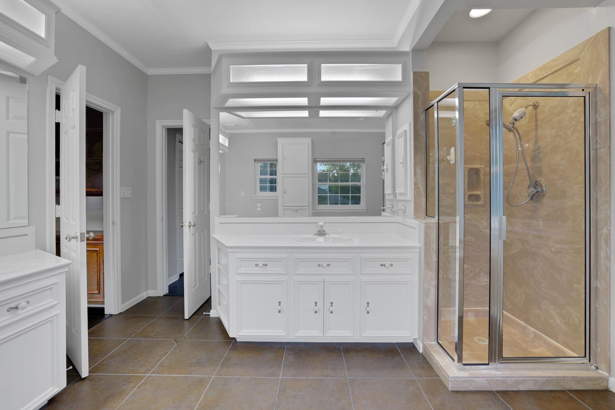 Bathroom with a white vanity, mirrored wall, and glass-enclosed beige-tile shower.