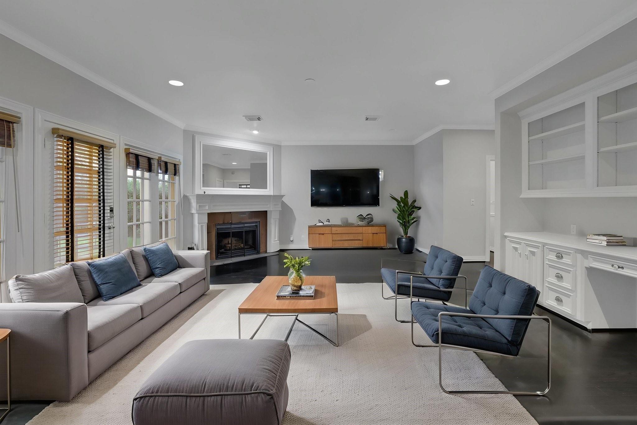 Living room with a fireplace, wall-mounted TV, tall windows, and gray and blue seating.