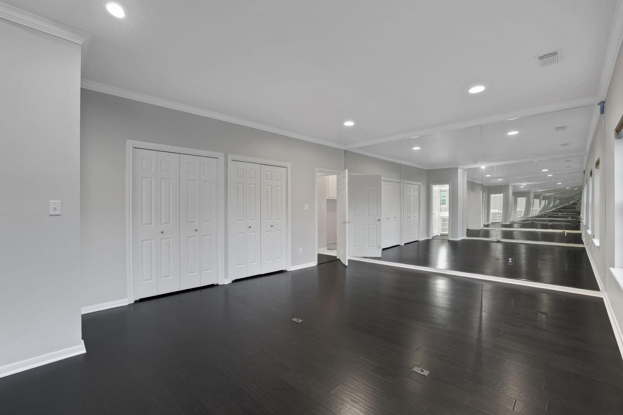 Empty exercise room with dark flooring, closet doors, and a wall of mirrors.