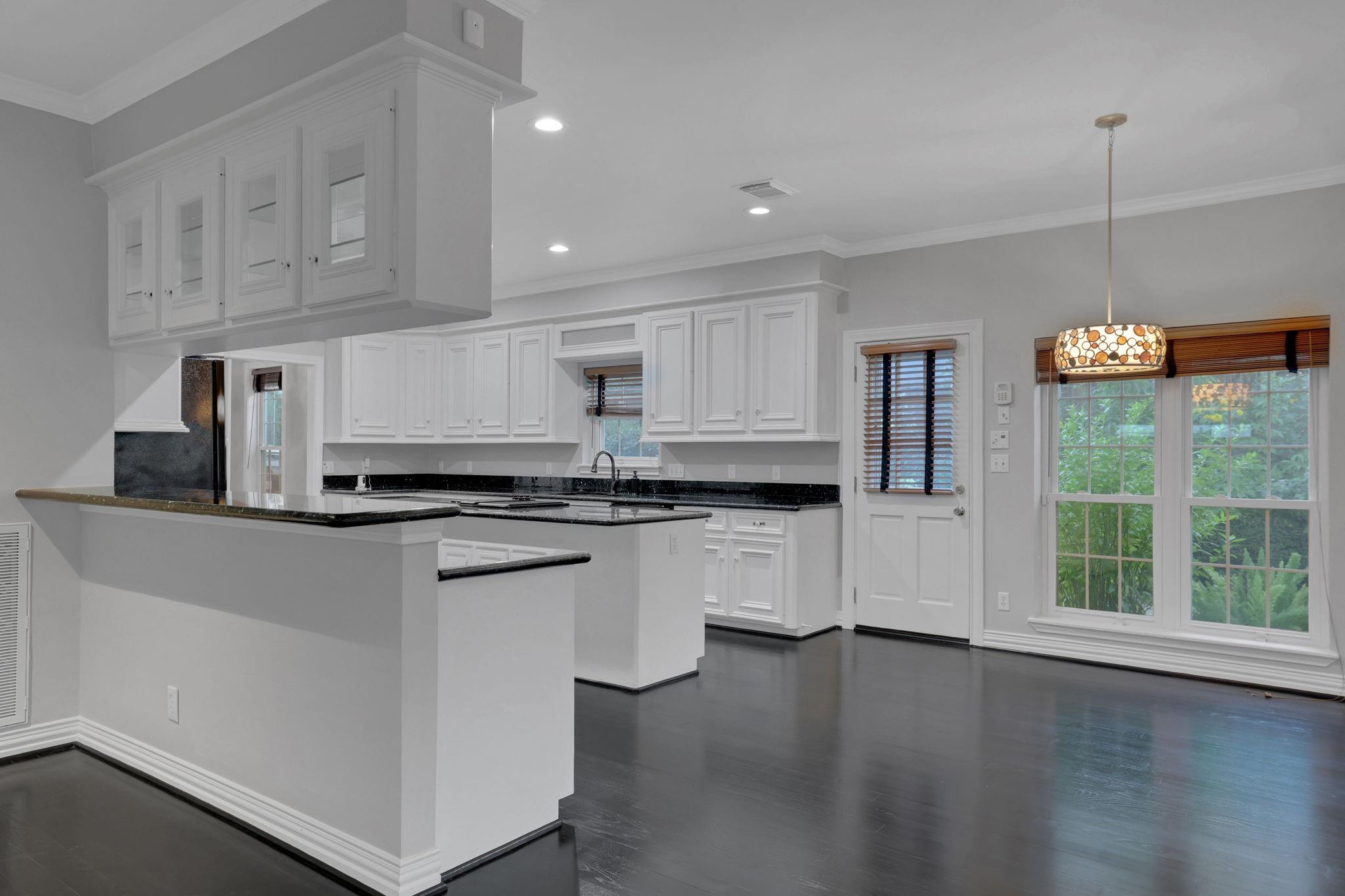 Kitchen with white cabinetry, black counters, a large breakfast bar, and windows overlooking greenery.
