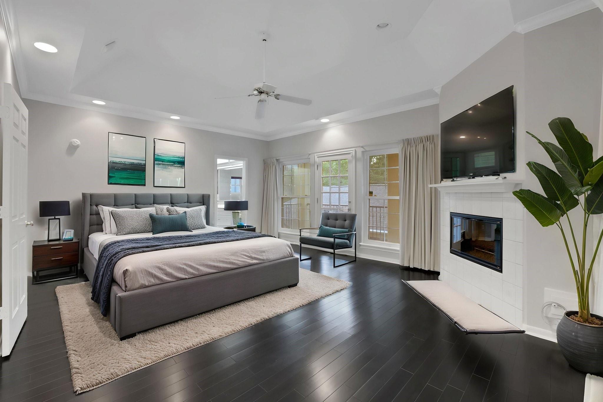 Staged bedroom with a large upholstered bed, fireplace, television, and French doors.