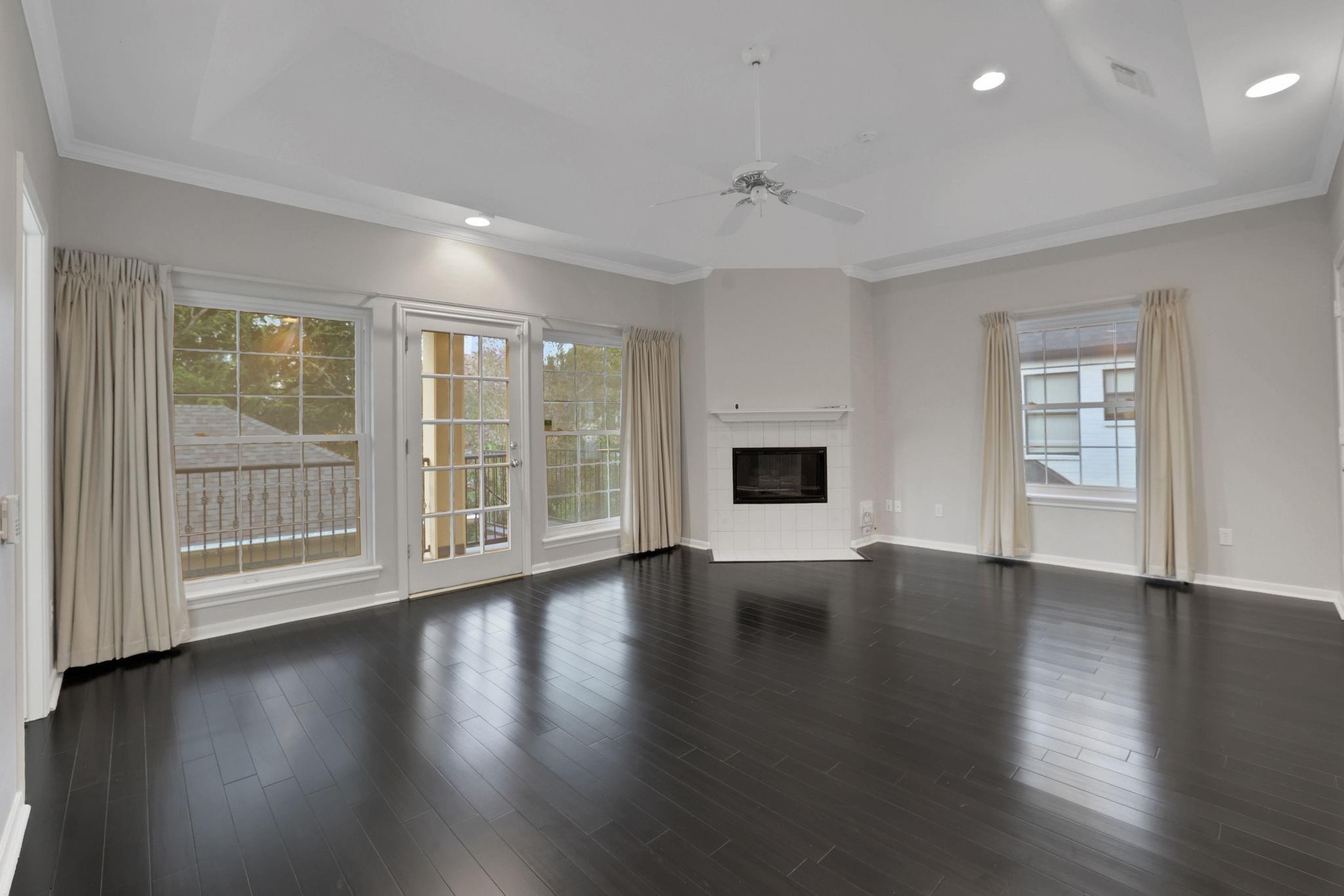 Unfurnished living room with dark wood floors, a tiled fireplace, and a tray ceiling.