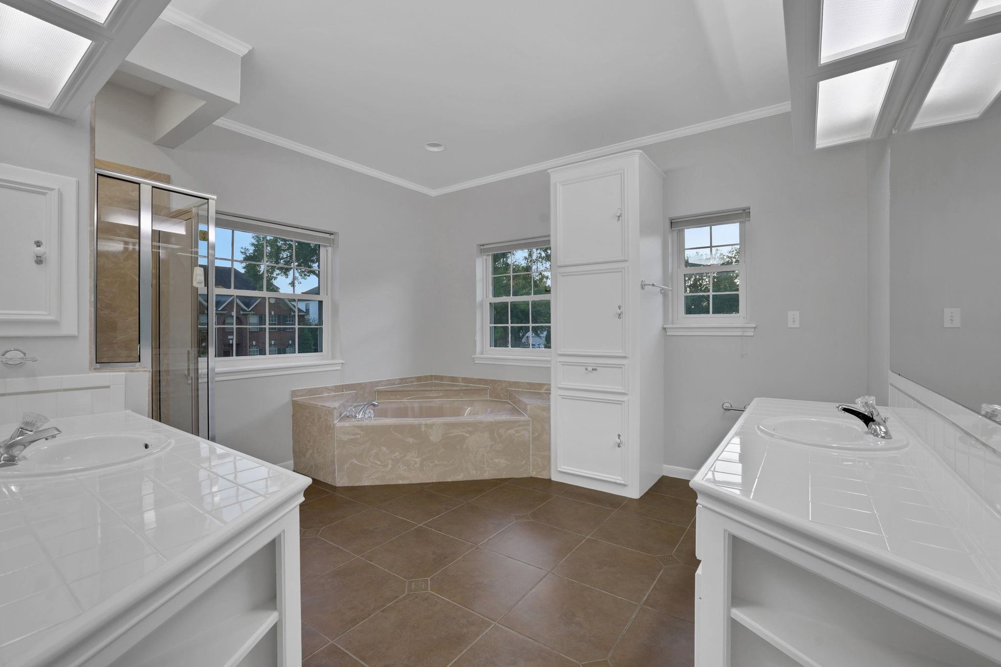 Bathroom with dual tiled vanities, a corner soaking tub, glass shower, and skylights.