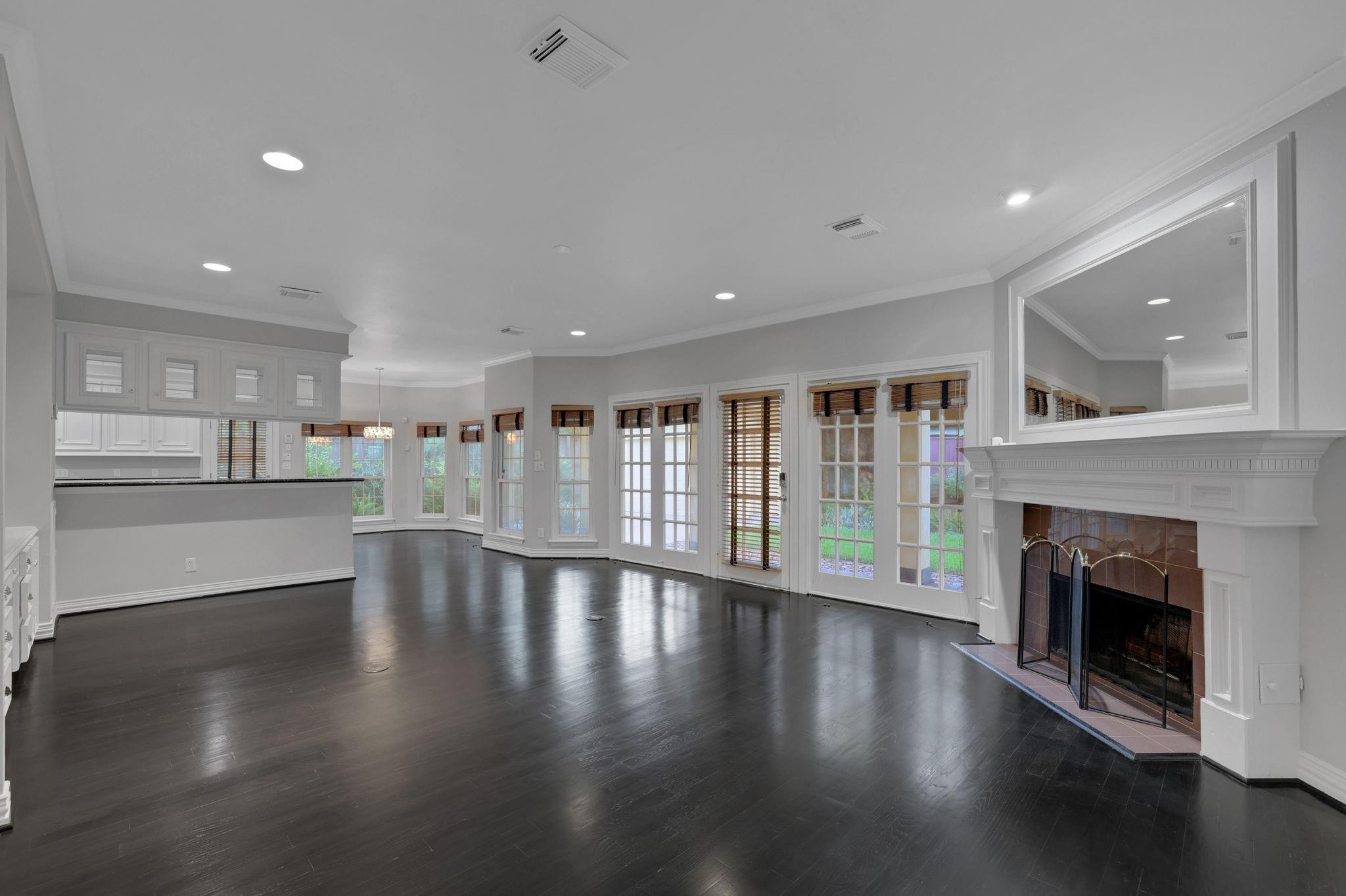 Open living area with dark hardwood floors, French doors, and a white fireplace beside the kitchen.