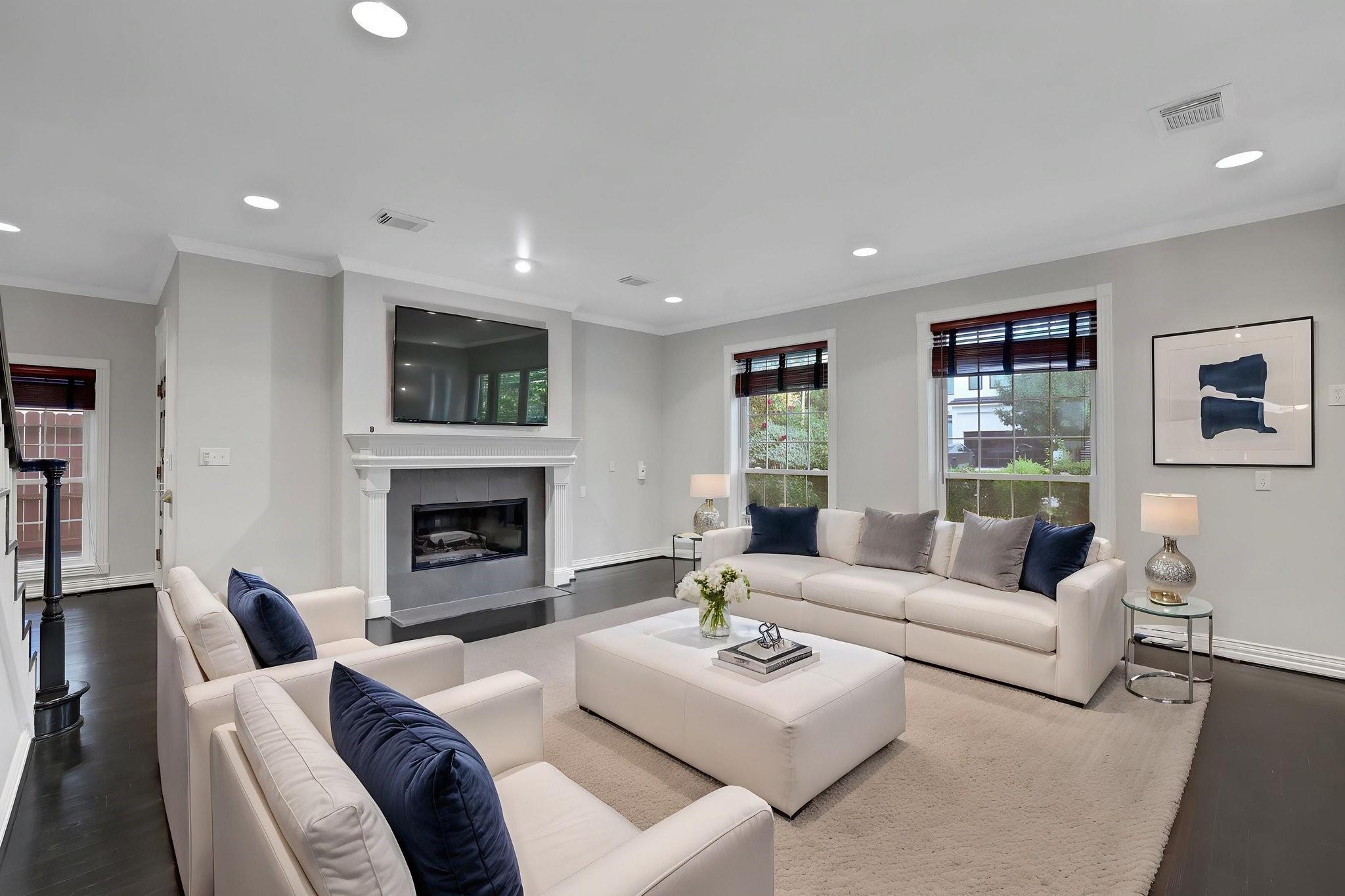 Living room with a white fireplace, wall-mounted television, cream sofas, and navy accent pillows.