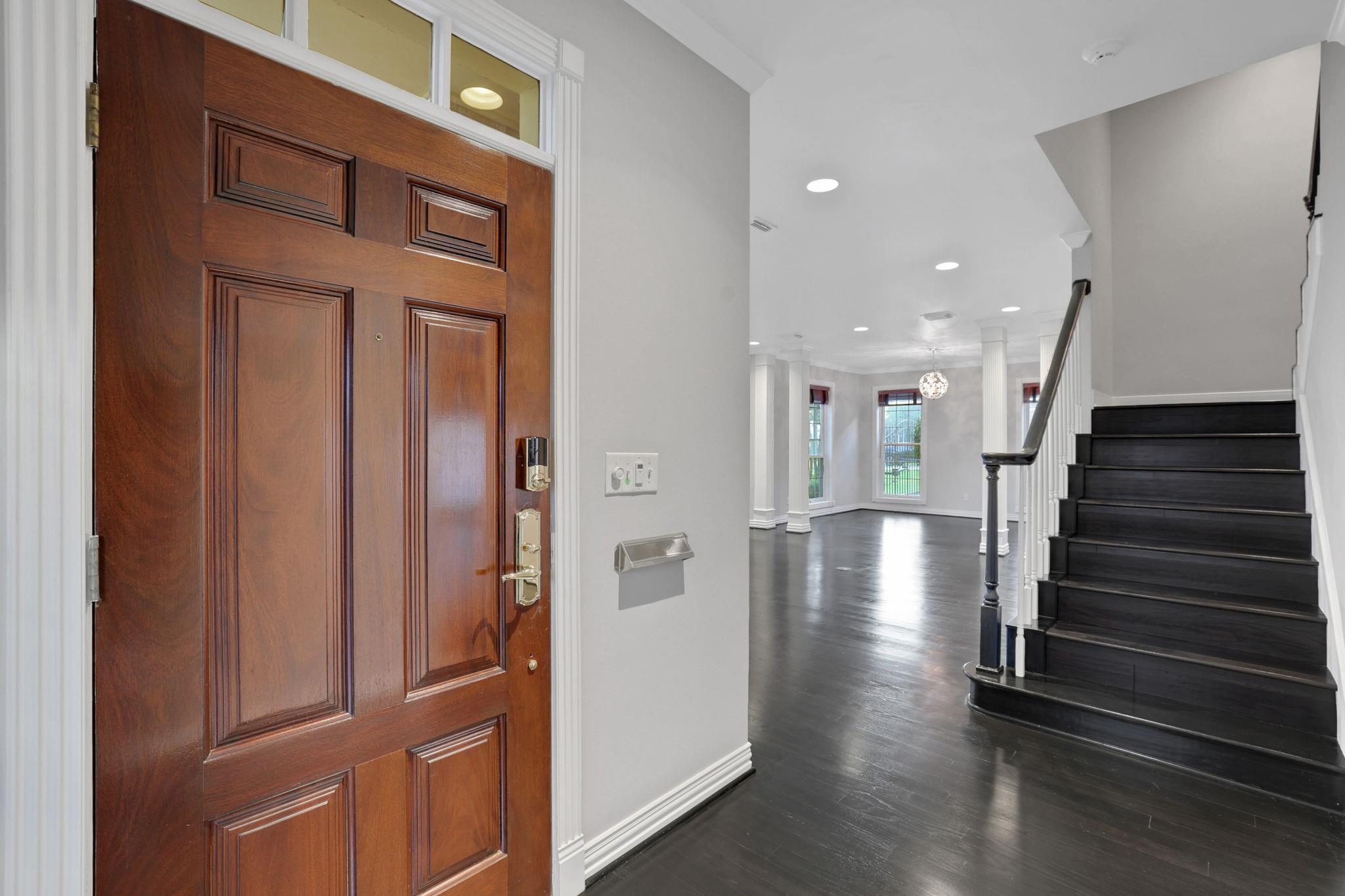 Entry foyer with a paneled wood front door, dark floors, and a staircase.