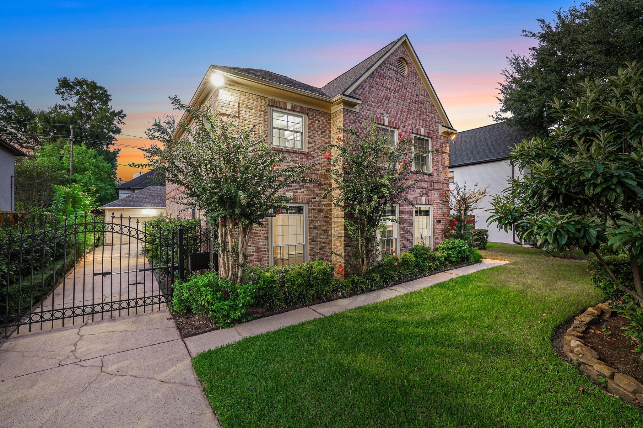 Two-story brick house with a steep gable, landscaped front yard, and gated driveway at dusk.