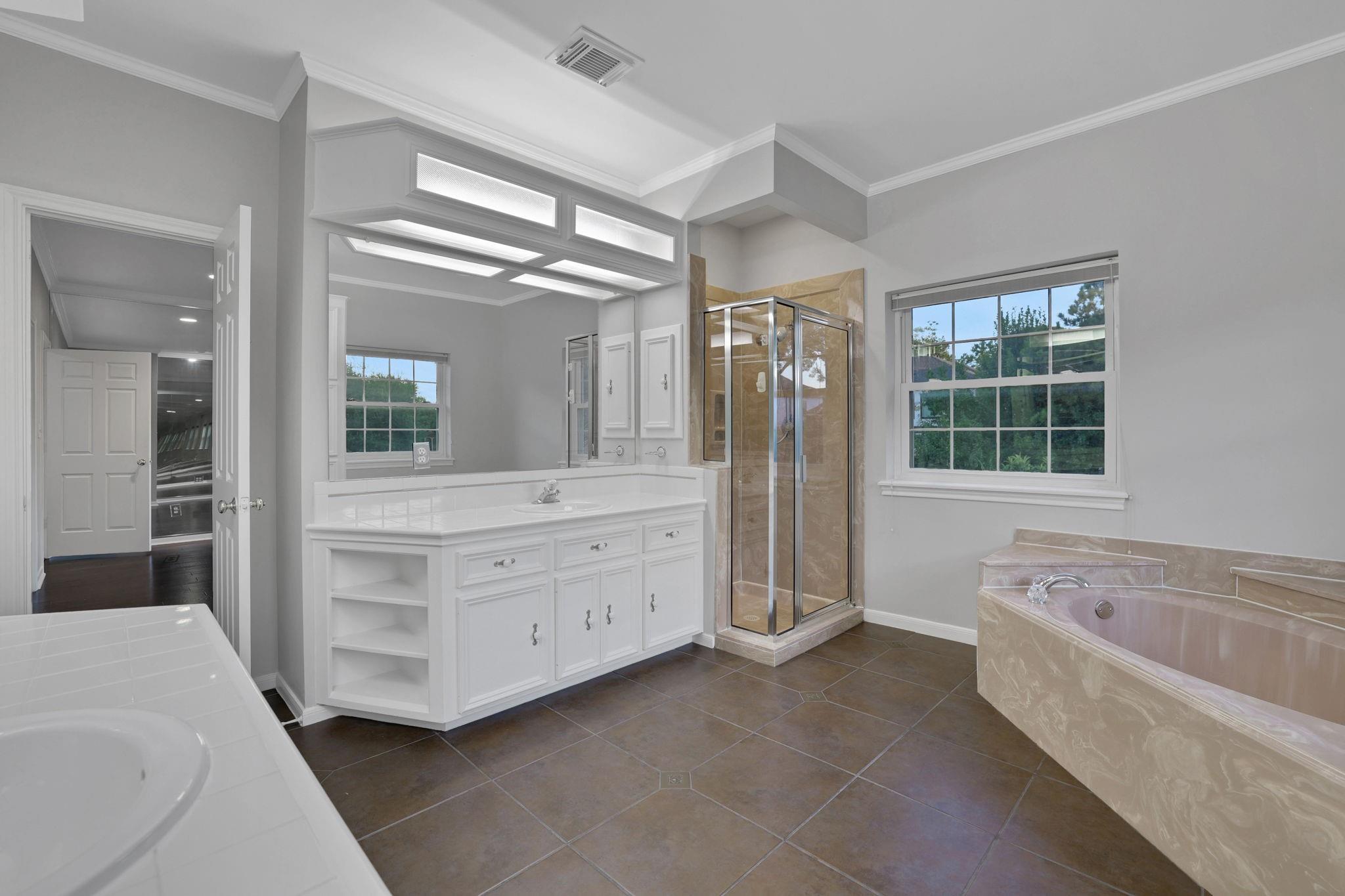 Bathroom with a long white vanity, glass shower, and corner soaking tub.