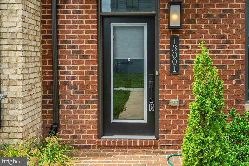 Brick building entrance with black-framed glass door and vertical 13001 address plaque.