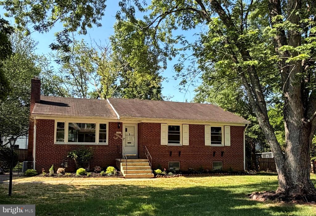 Red brick ranch house with white shutters, front steps, and mature shade trees.