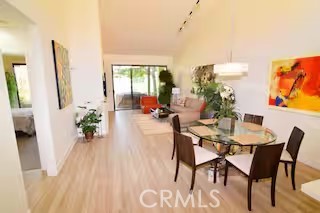 Open-plan dining and living area with a glass table, dark chairs, and large windows.